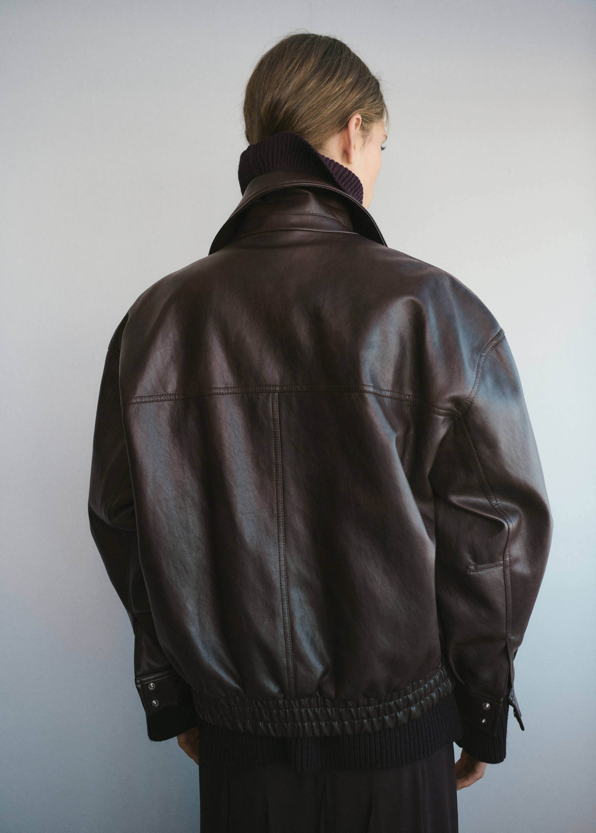 Dark brown oversized jacket with a pointed collar, back seaming and a ribbed hem, seen from behind.