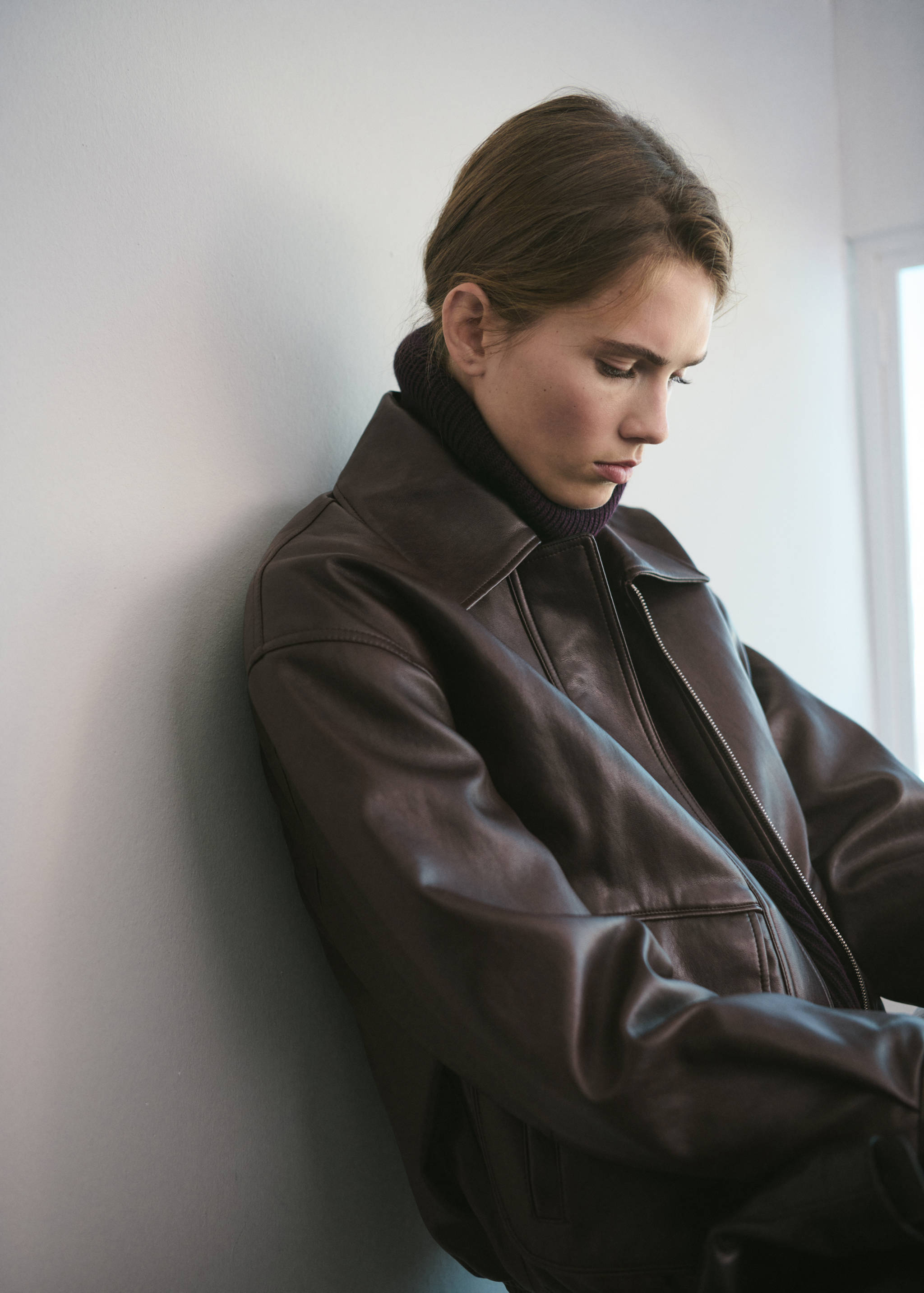 Dark brown jacket with a wide collar and front zip, worn over a ribbed turtleneck.