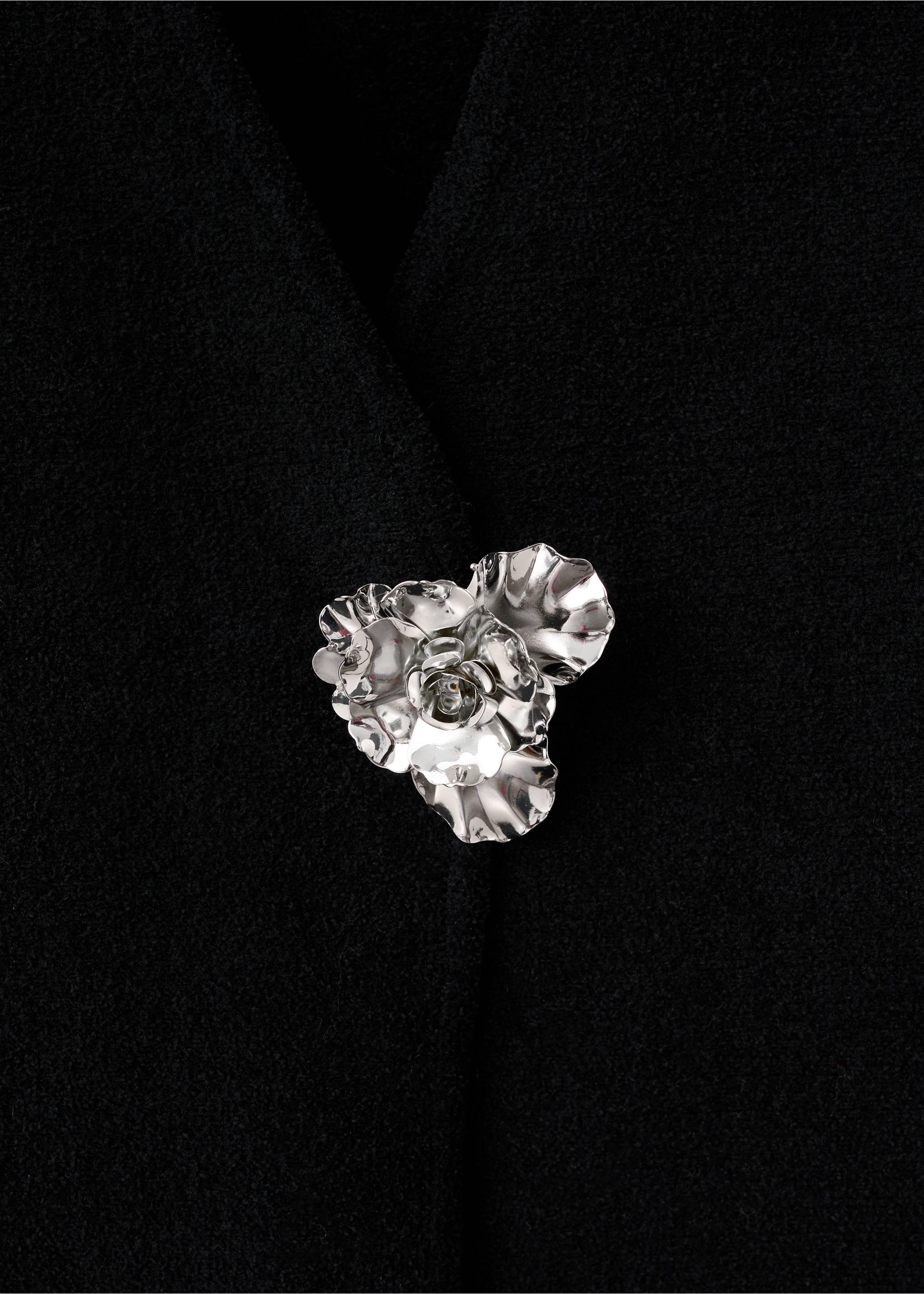 Close-up of a black jacket with a metallic silver floral closure., Black. Ref: 17099103-00.