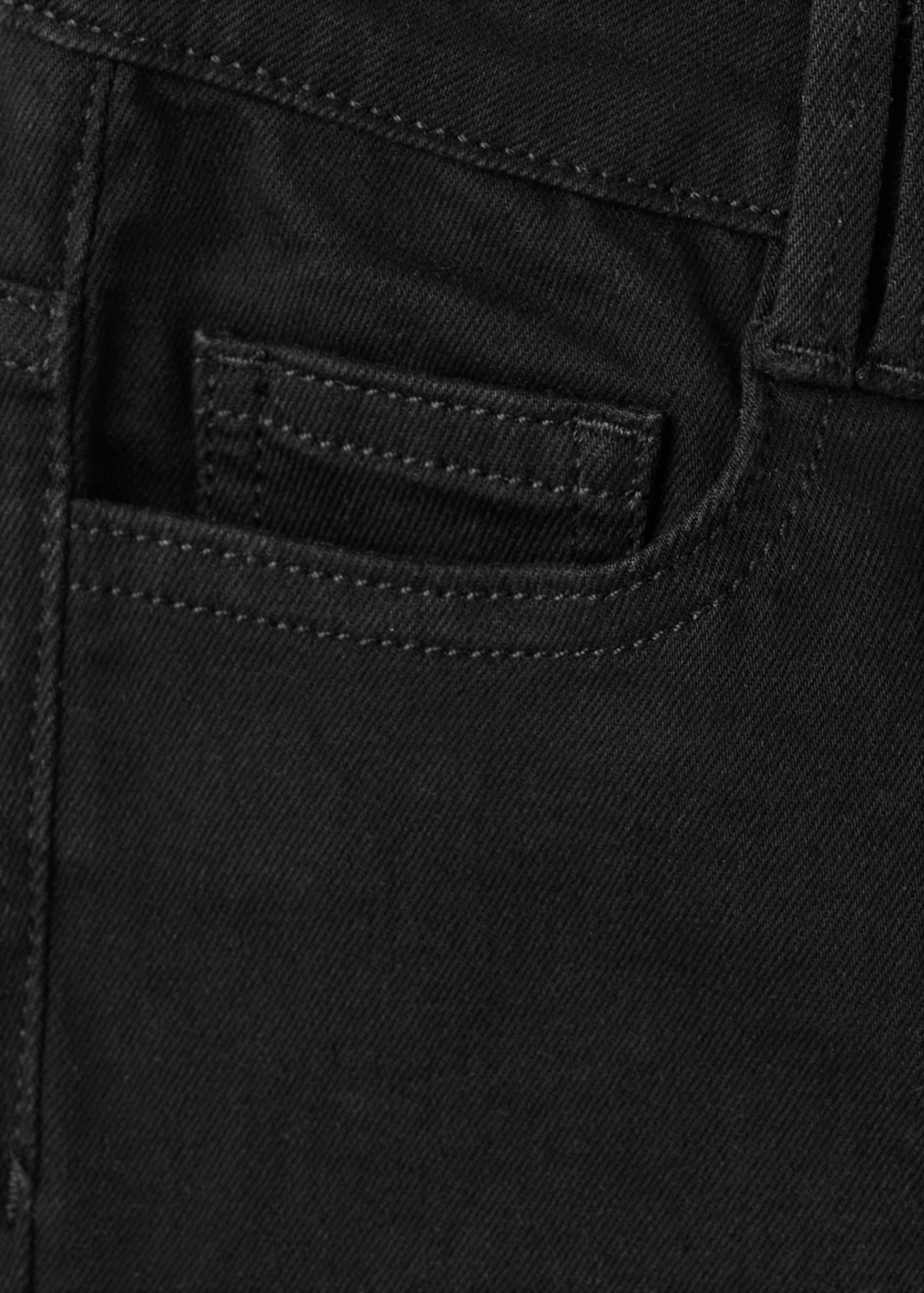 Close-up of black denim trousers fabric and pocket detail.