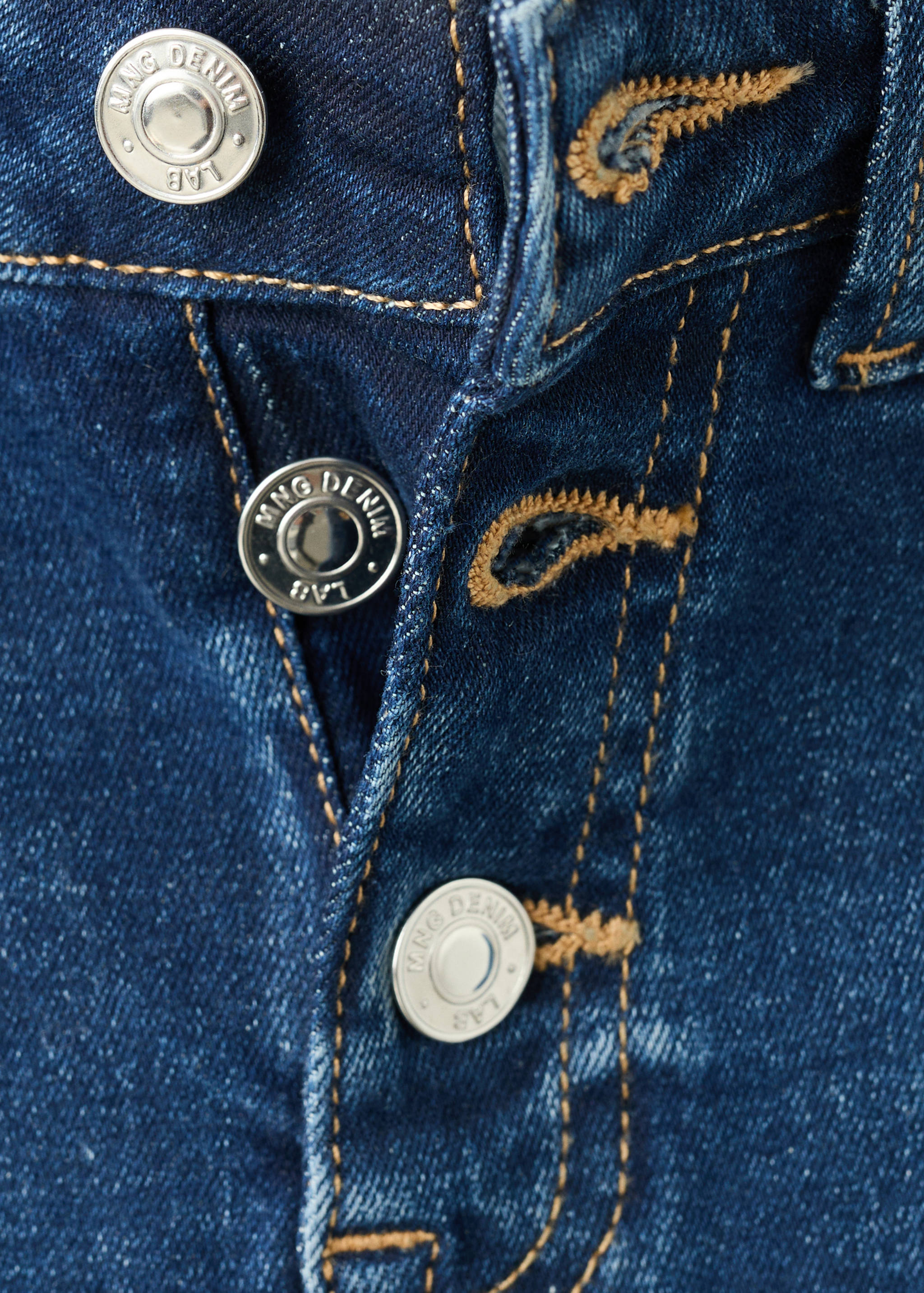 Close-up of blue denim trousers showing the button fly and contrast topstitching.