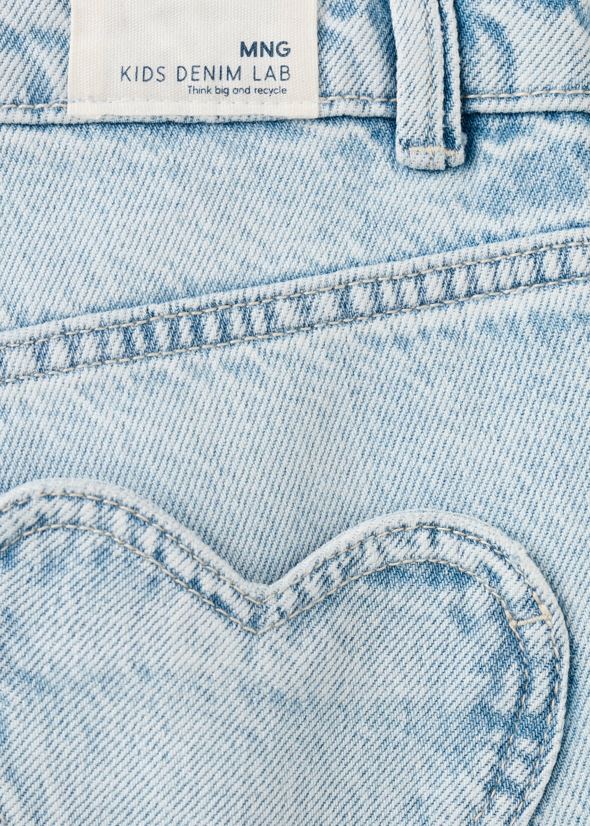 Close-up of light-wash denim trousers featuring a heart-shaped pocket and branded label.