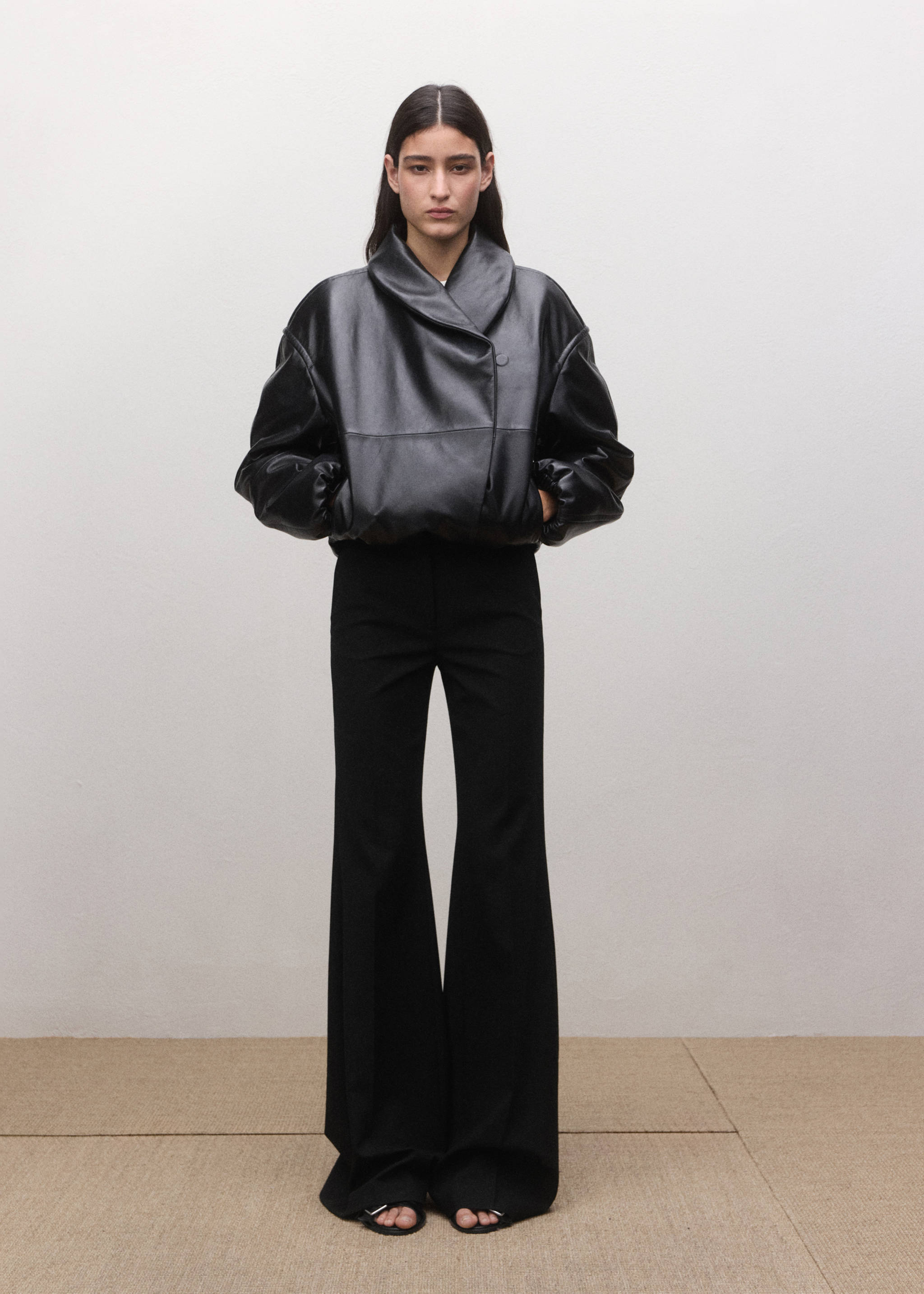 Black flared trousers worn with a voluminous black leather jacket.