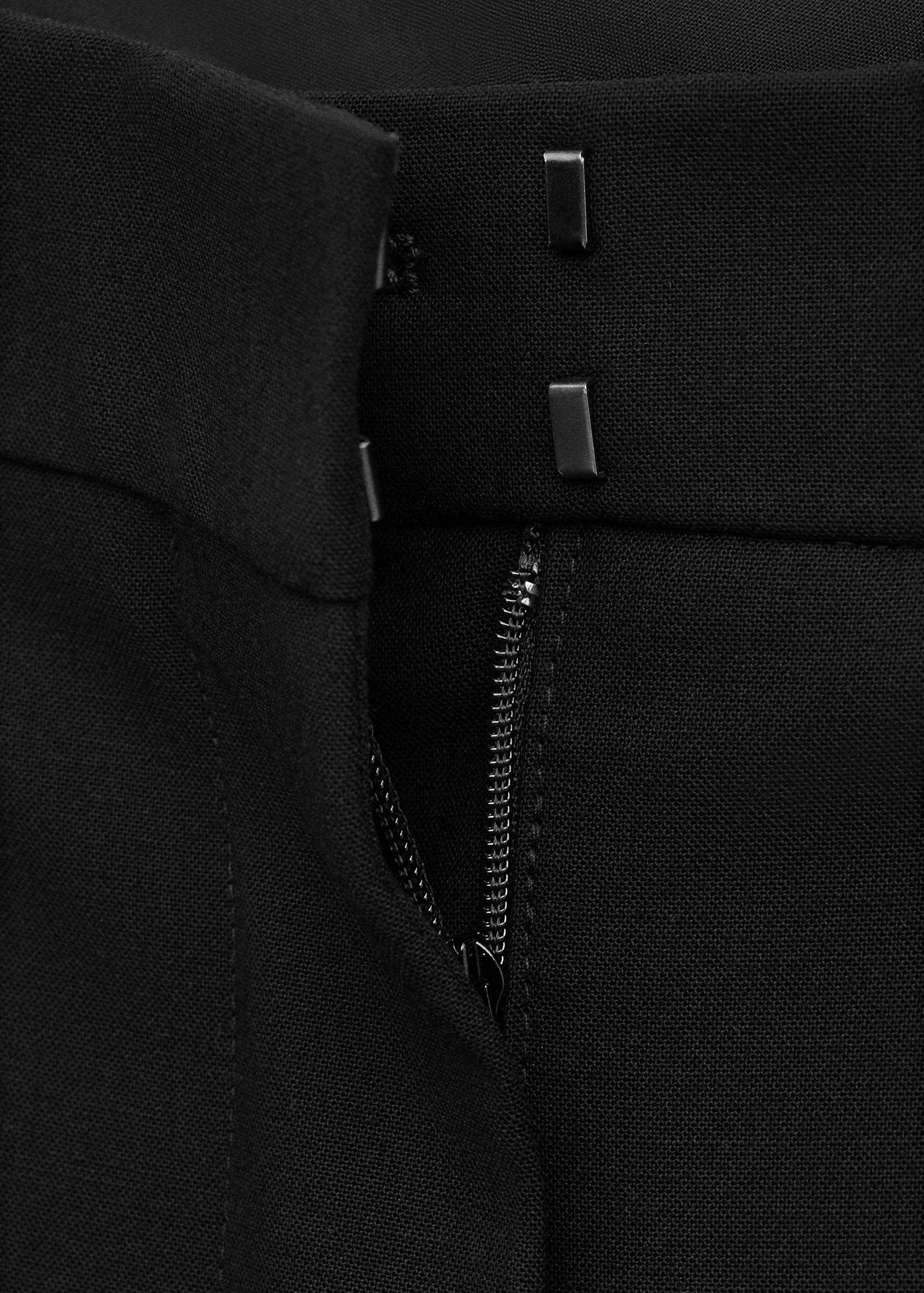 Close-up of black trousers showing the waistband and hook-and-eye fastening.