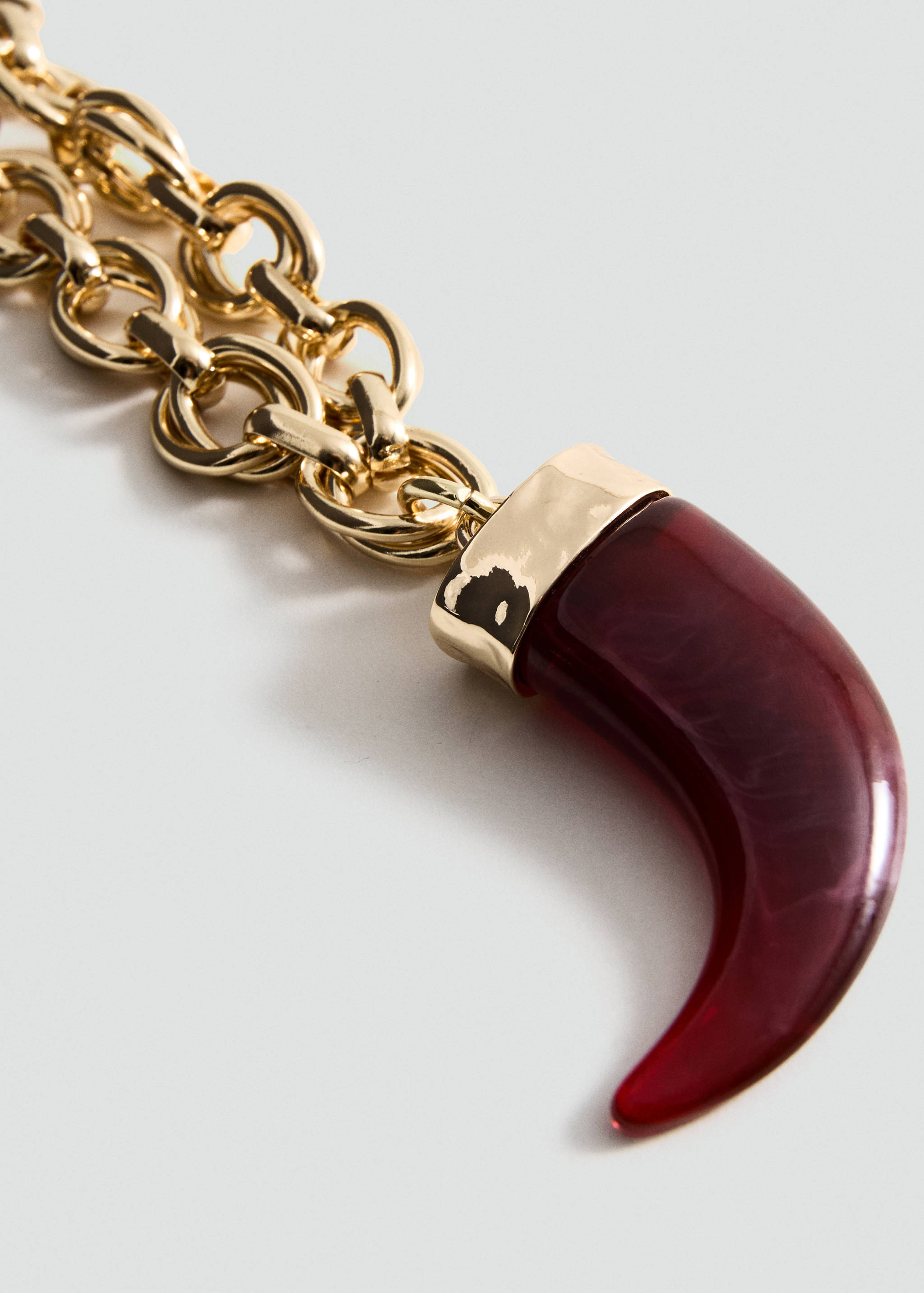 Gold-tone chain necklace featuring a curved burgundy resin tusk pendant.