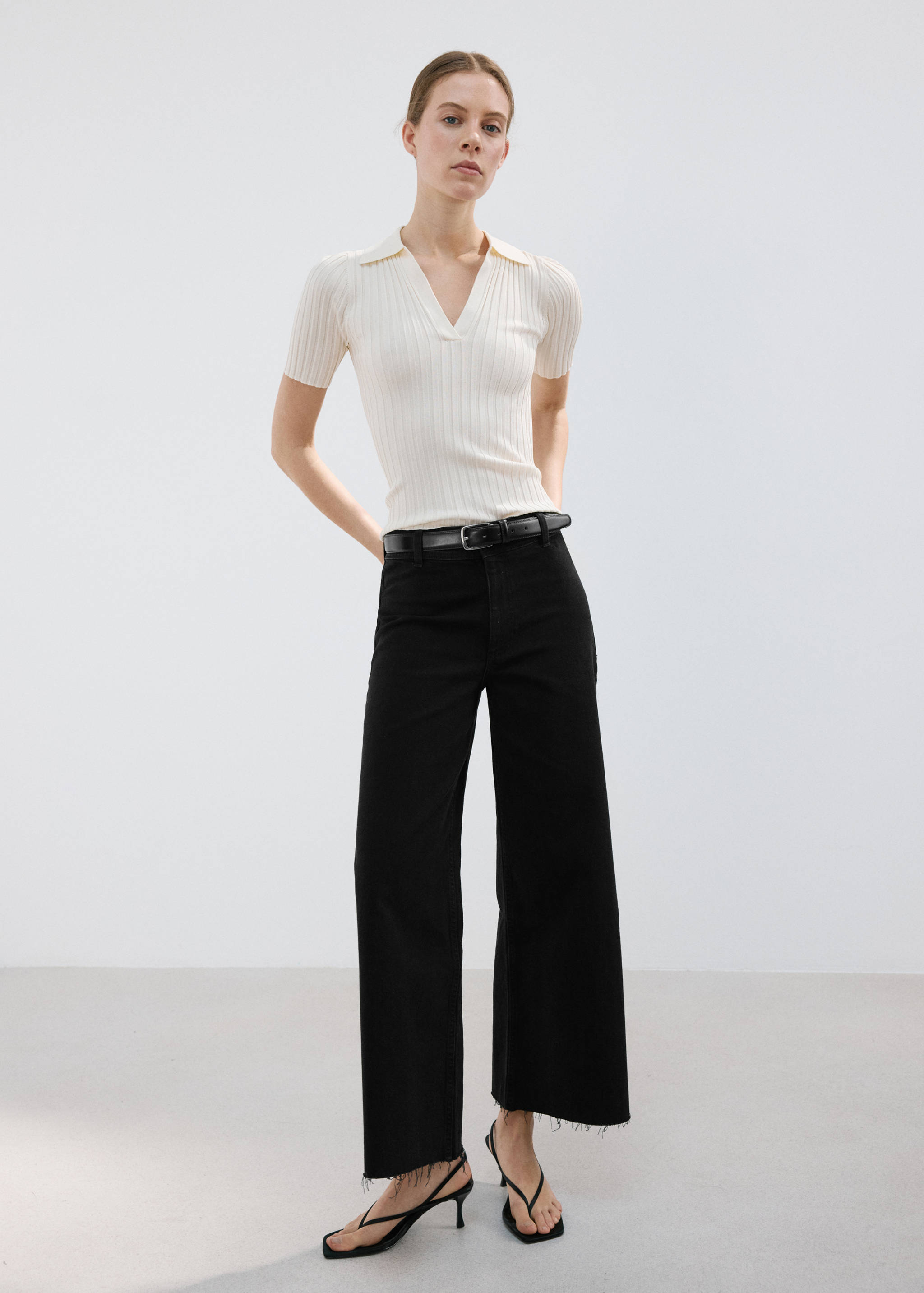 Black wide-leg denim trousers with a raw hem, worn with a cream ribbed polo top.
