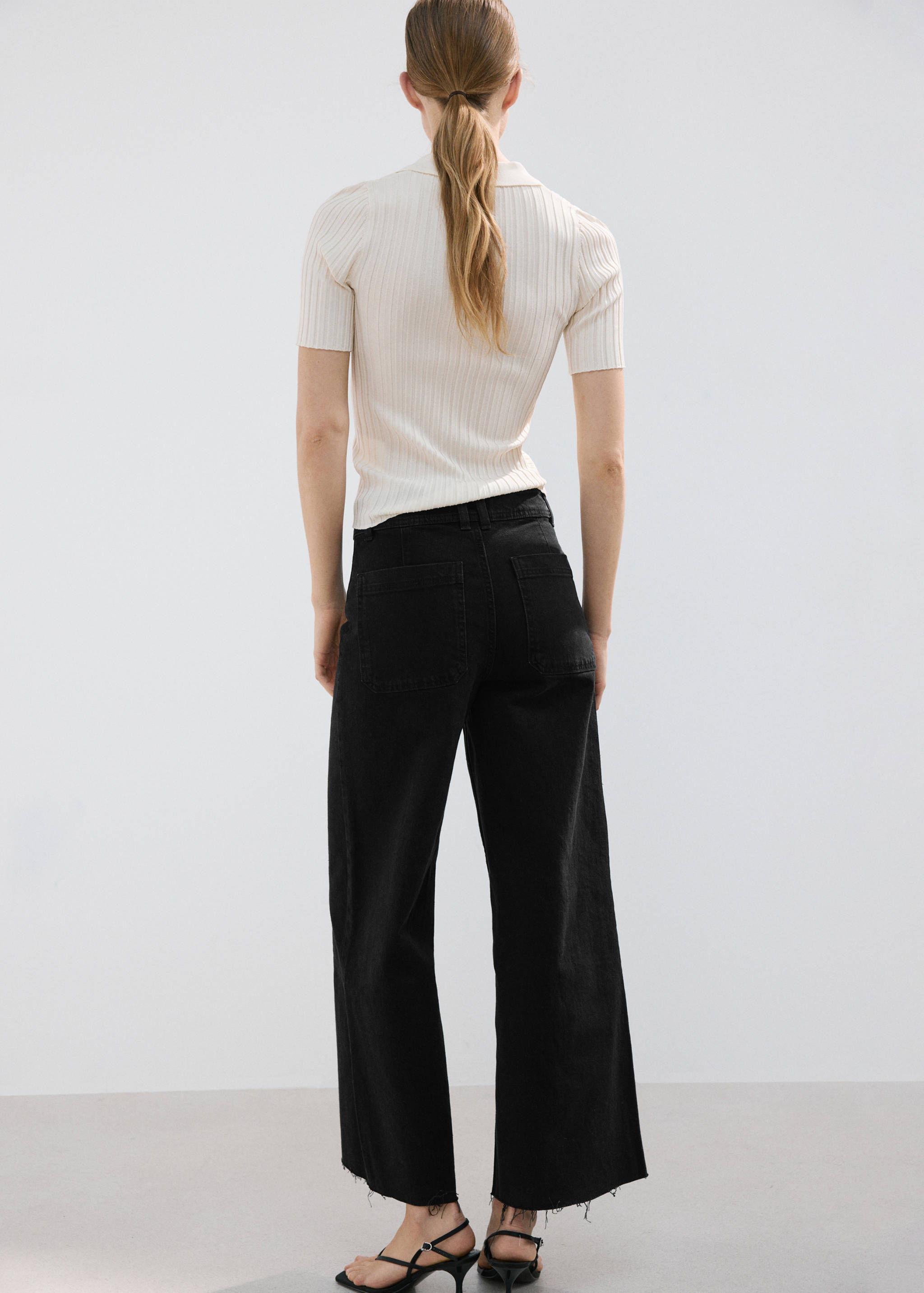 Back view of black denim trousers worn with a cream ribbed top.