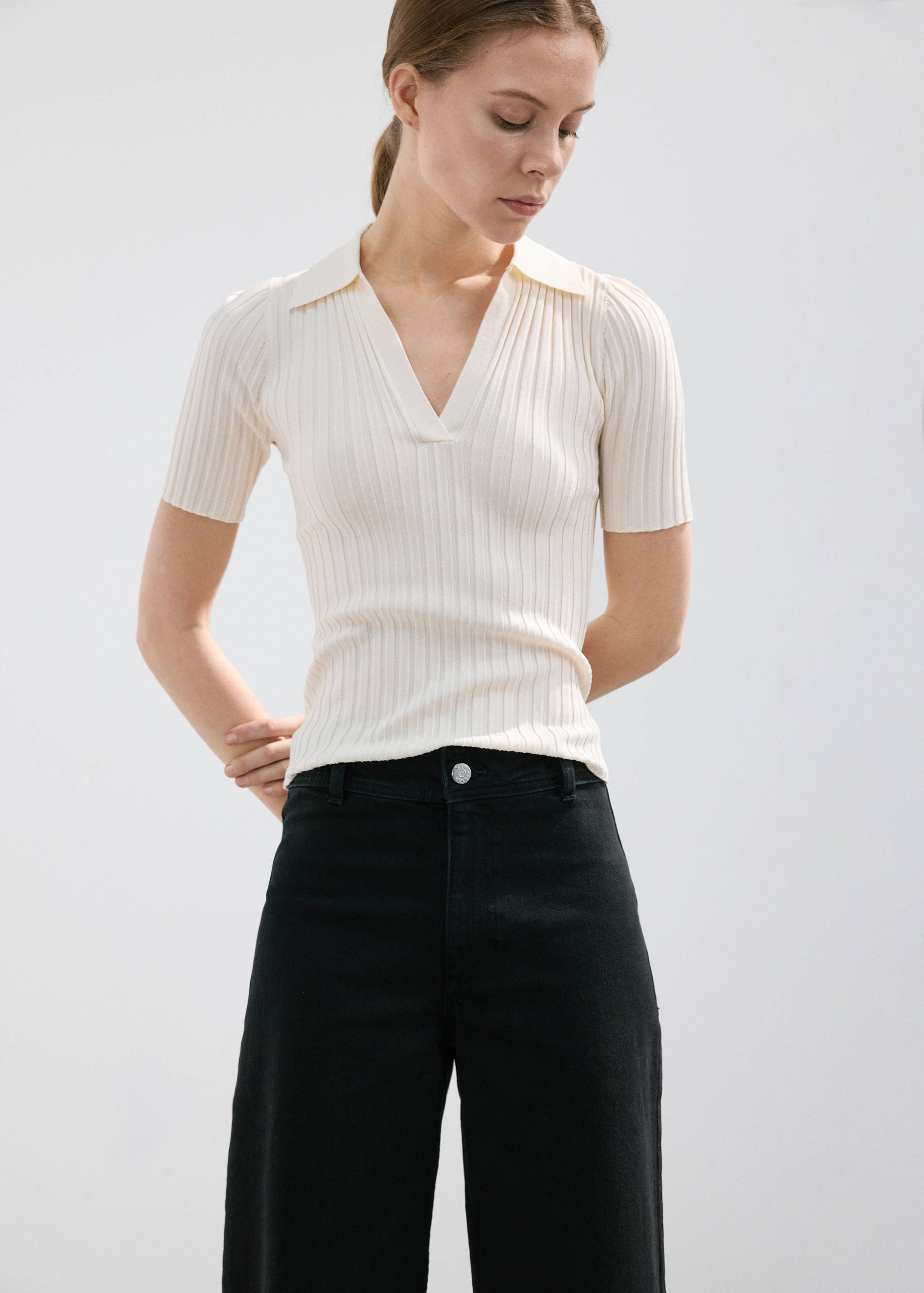 Black high-rise jeans with a visible button fastening, paired with a cream ribbed polo top.