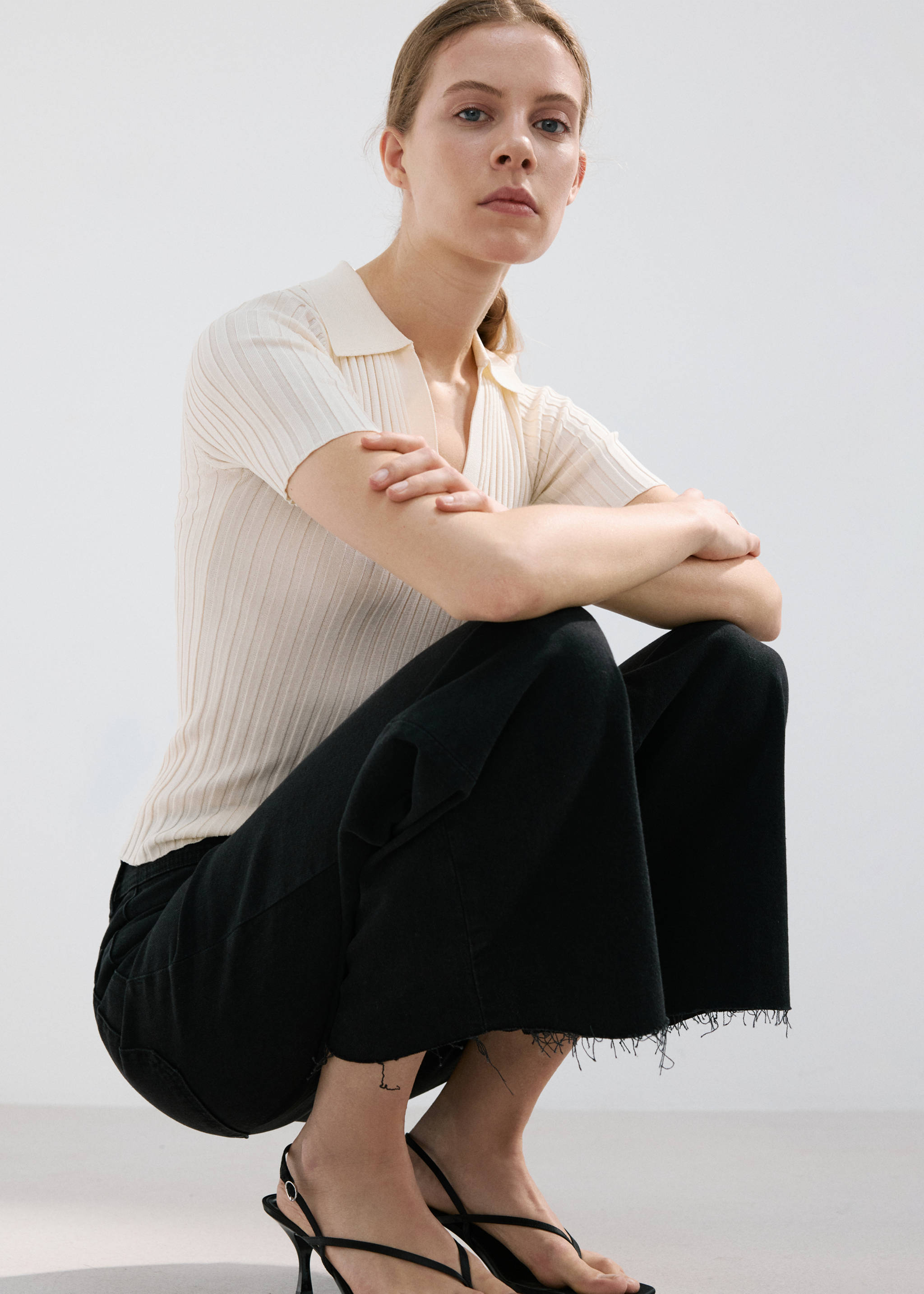 Black wide-leg jeans with frayed hems worn with a cream ribbed polo.