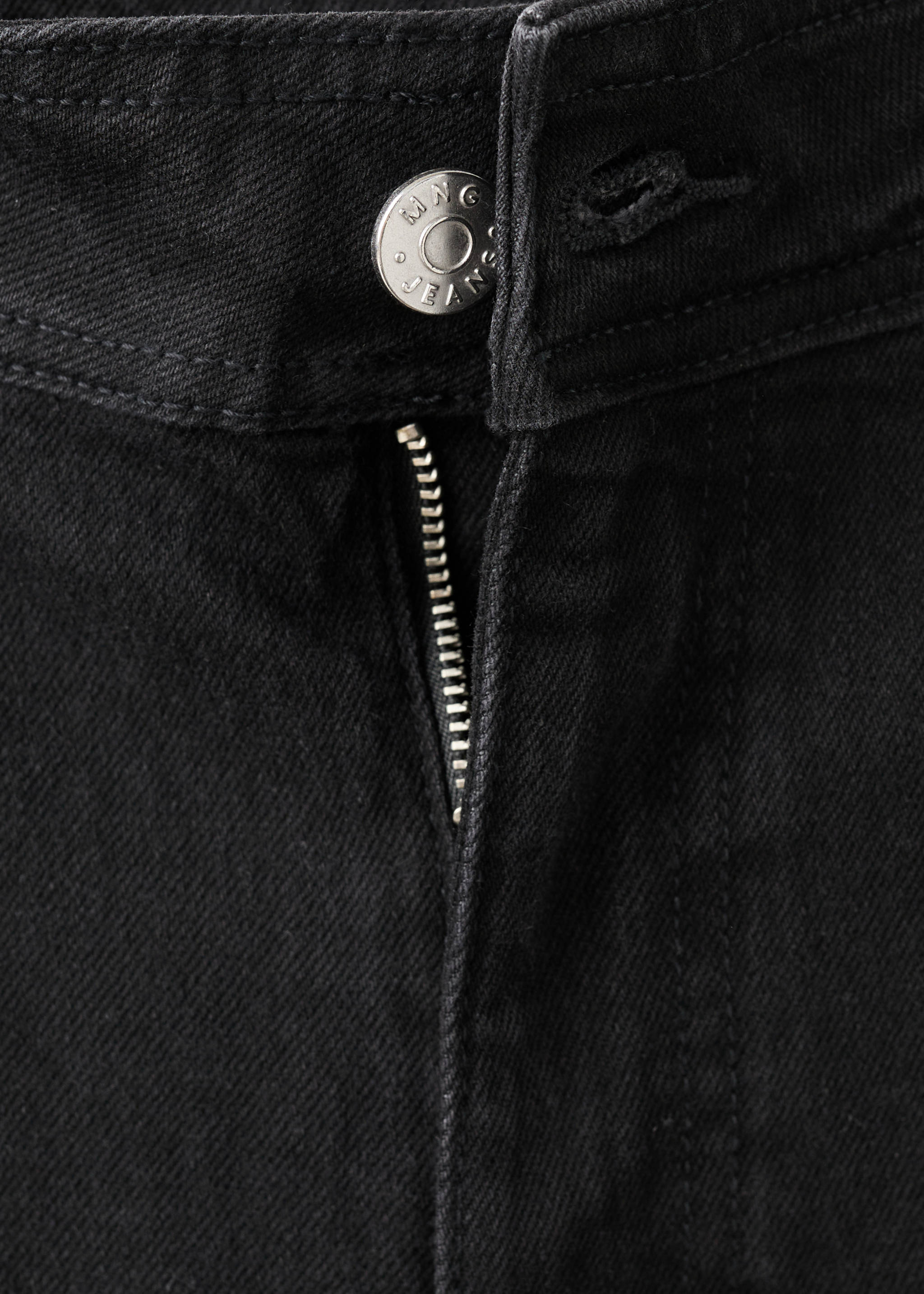 Close-up of the waistband and zip fly of black jeans with a branded button.