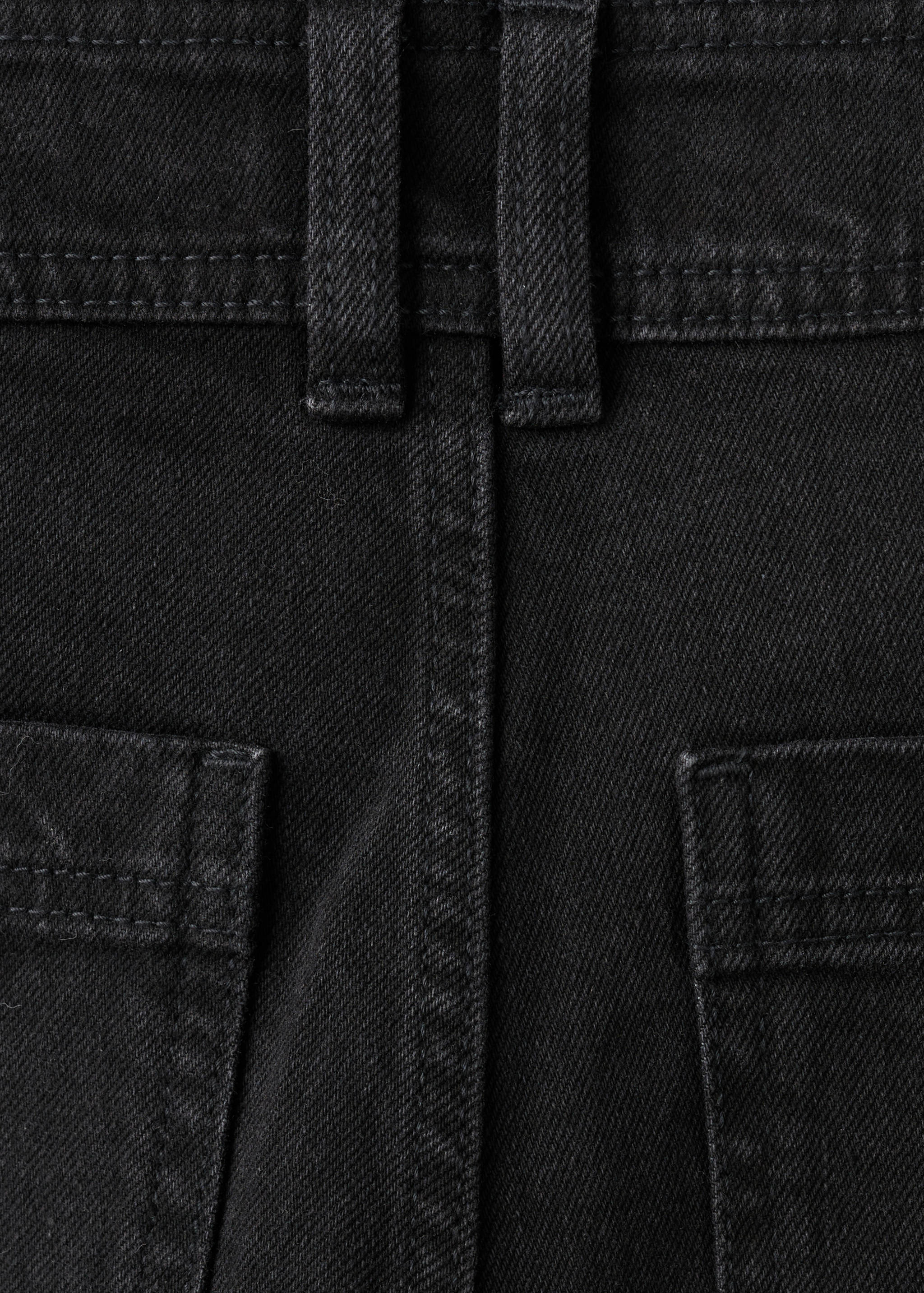 Close-up of black denim fabric, showing waistband, belt loops, and pockets.
