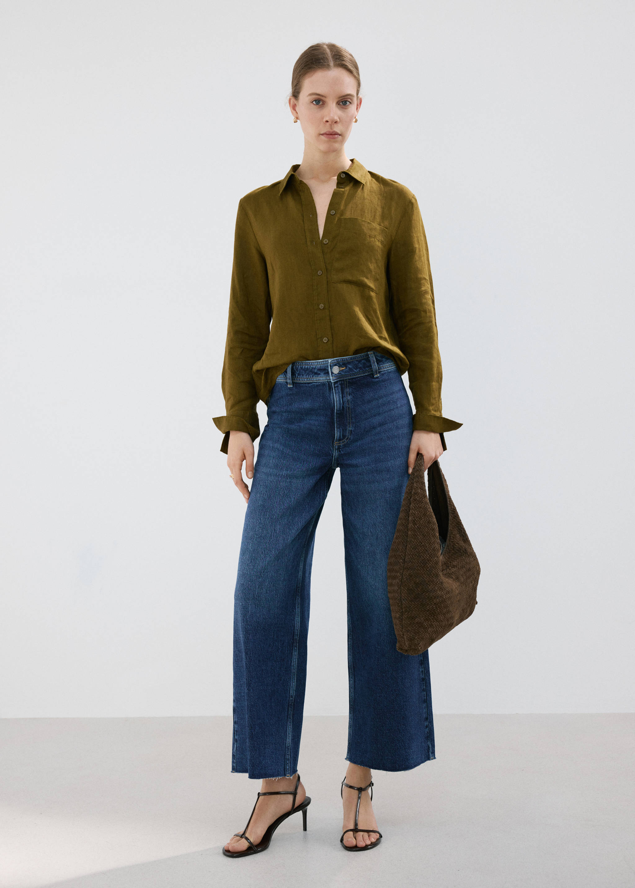 Dark blue denim trousers in a wide-leg cropped fit, worn with an olive green shirt and dark brown bag.