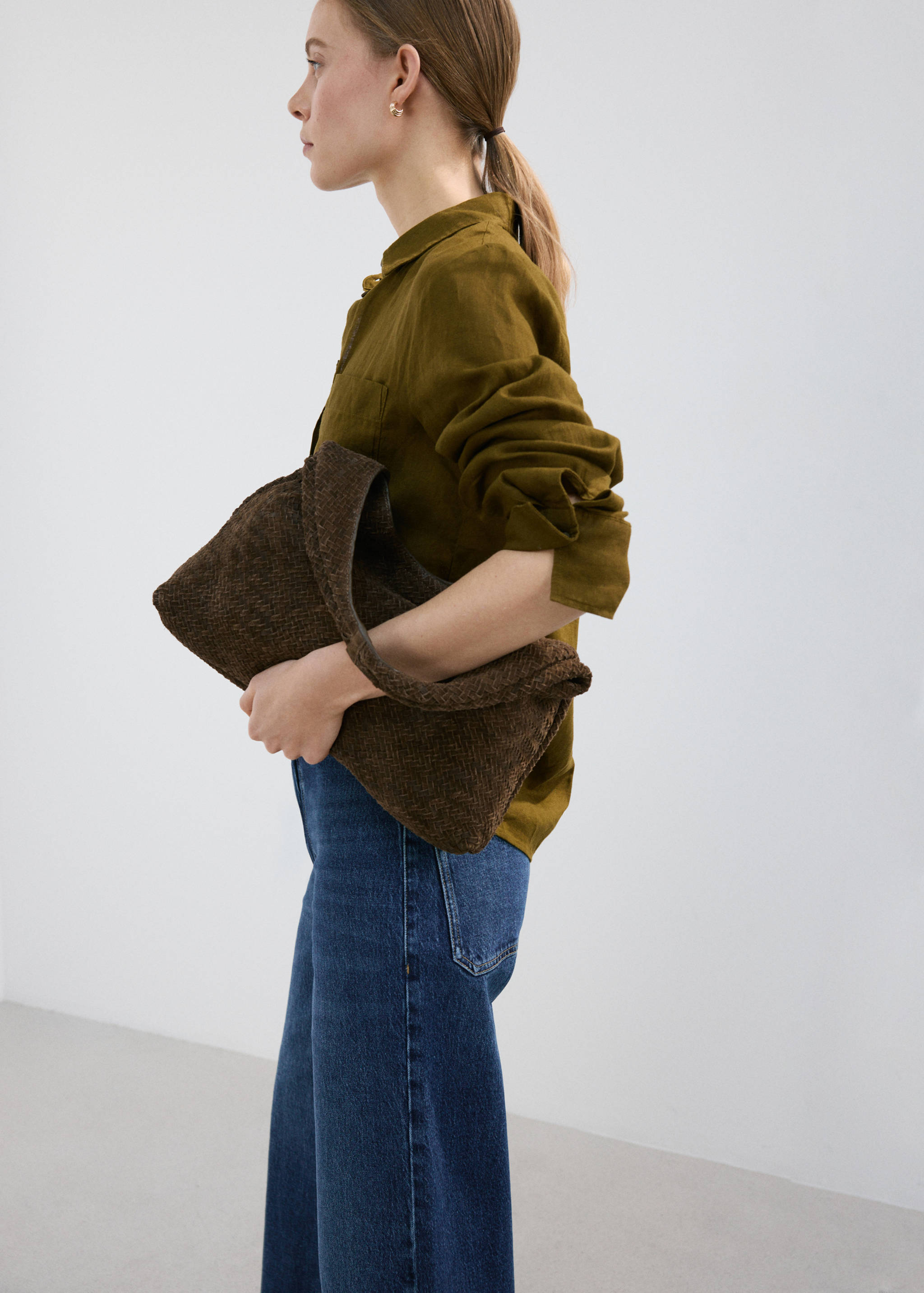 Blue jeans worn with an olive green shirt and a brown woven bag.