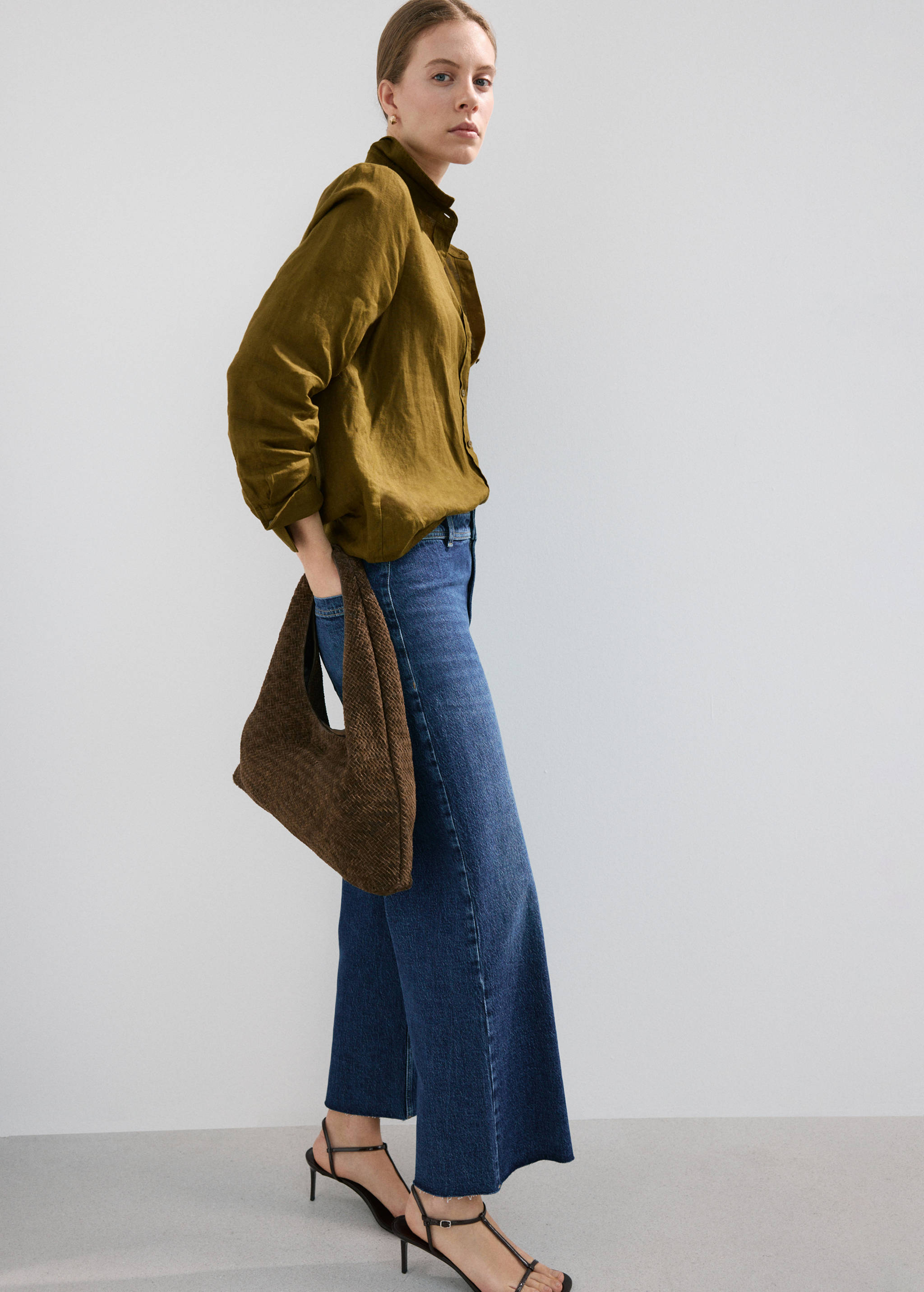 Blue denim trousers with a wide-leg silhouette and raw-hem cropped length, worn with an olive green shirt.