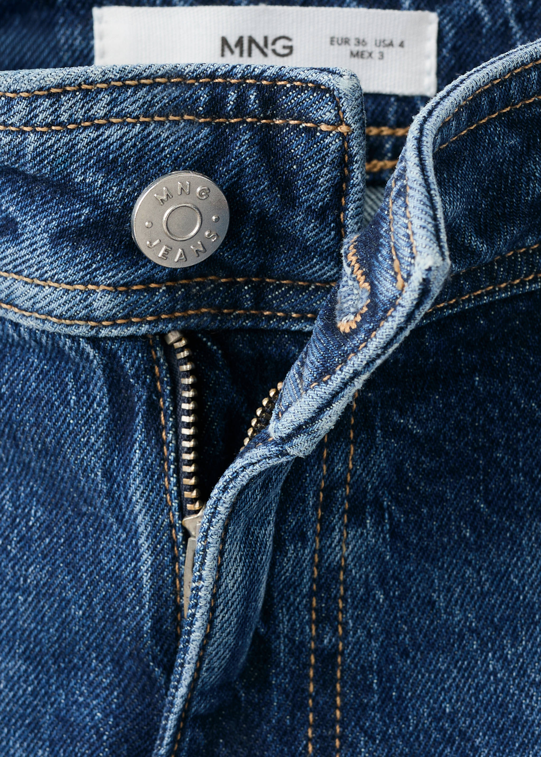 Close-up of blue denim trousers waistband, metal button, and zip fly.