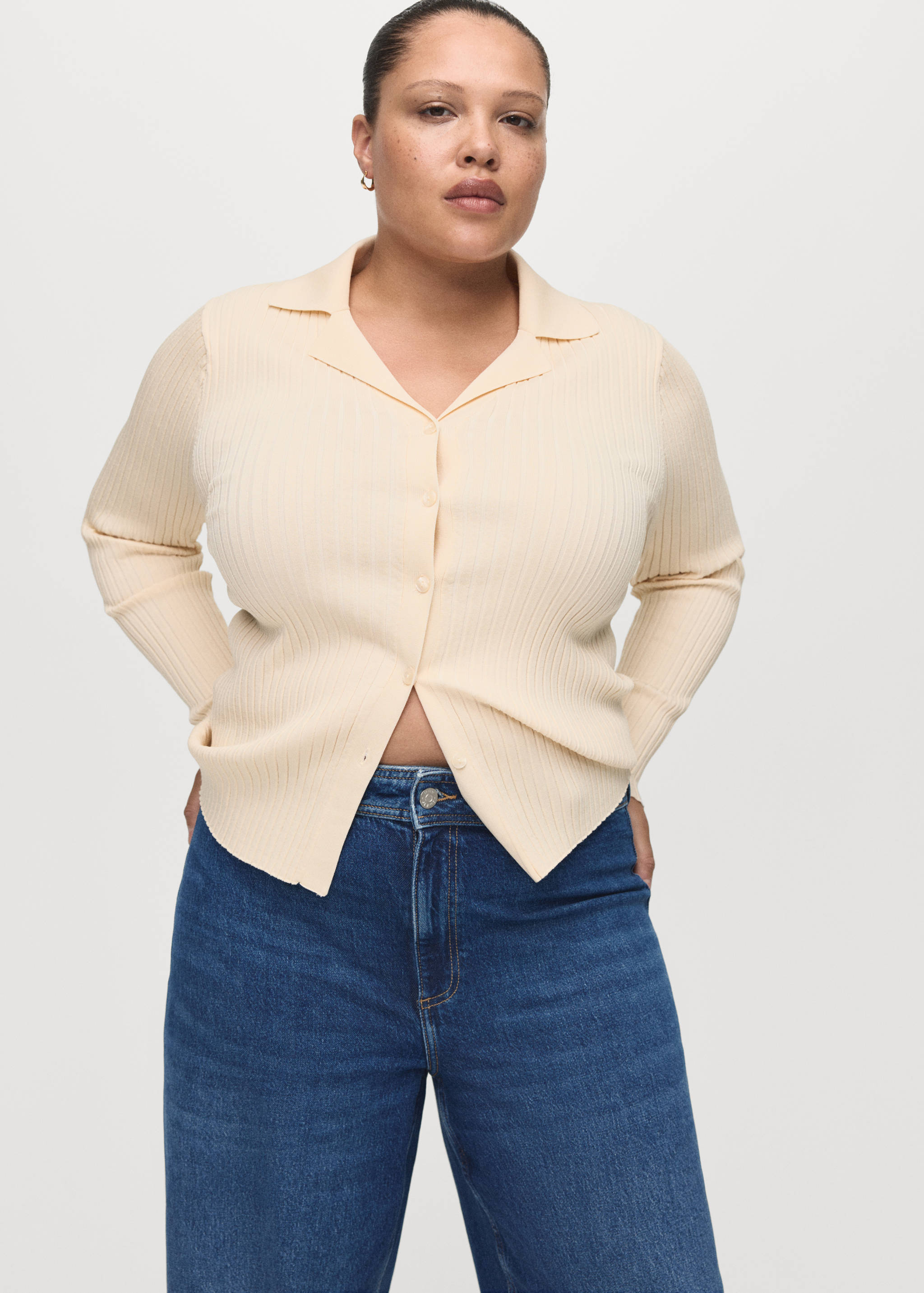 Pale yellow ribbed knit cardigan with a lapel collar and button fastening, worn with blue denim trousers.