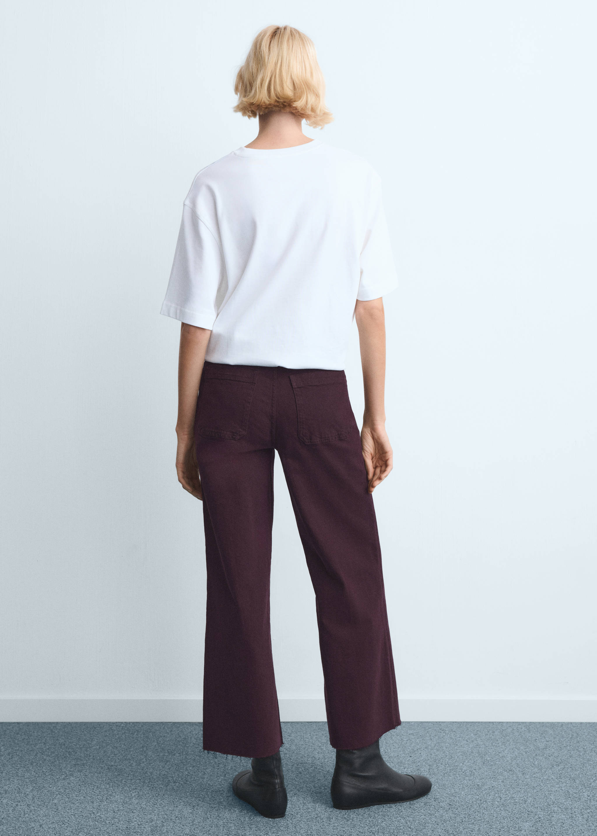 Burgundy denim trousers shown from the back, featuring patch pockets and raw-edge hems.