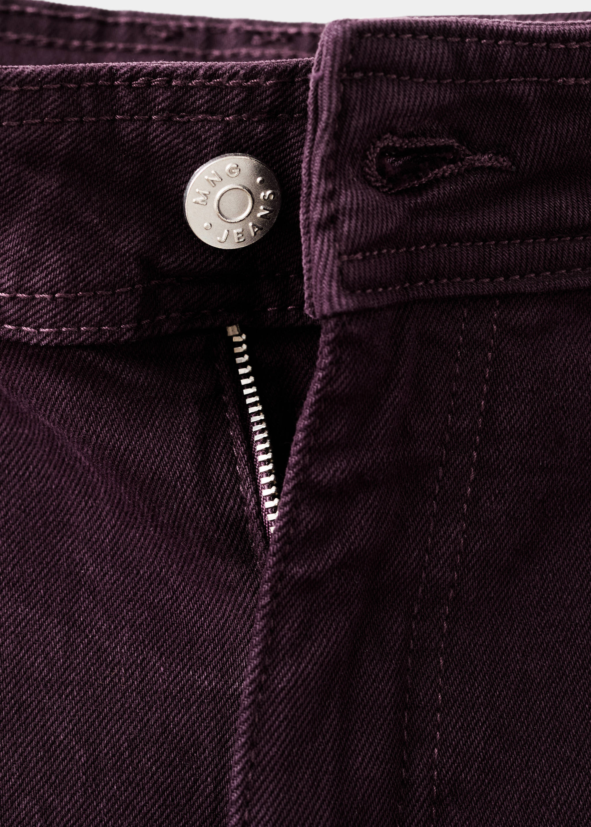 Close-up of dark plum purple denim jeans button and zip fly detail.