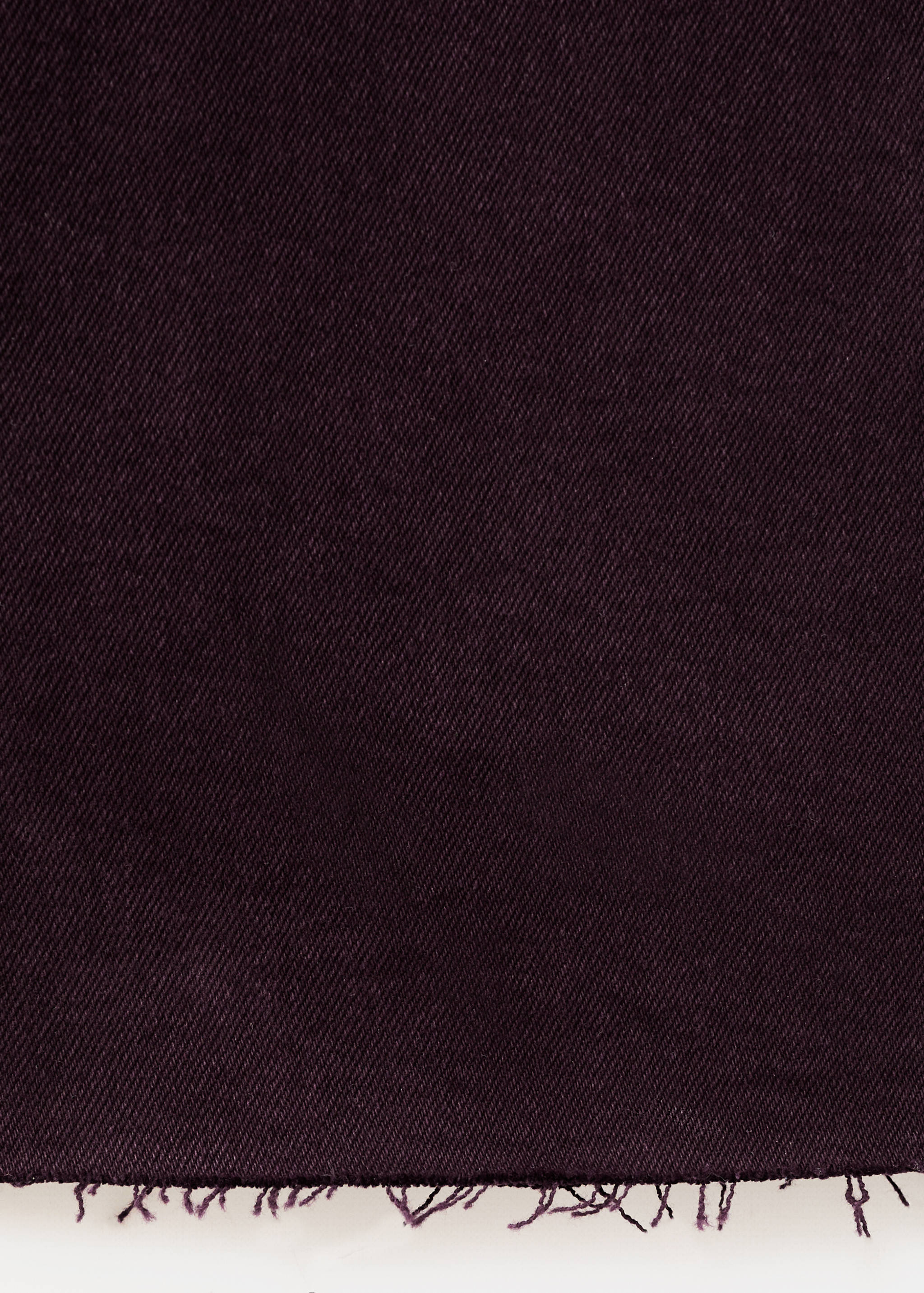 Close-up of dark burgundy denim fabric with a raw frayed hem.