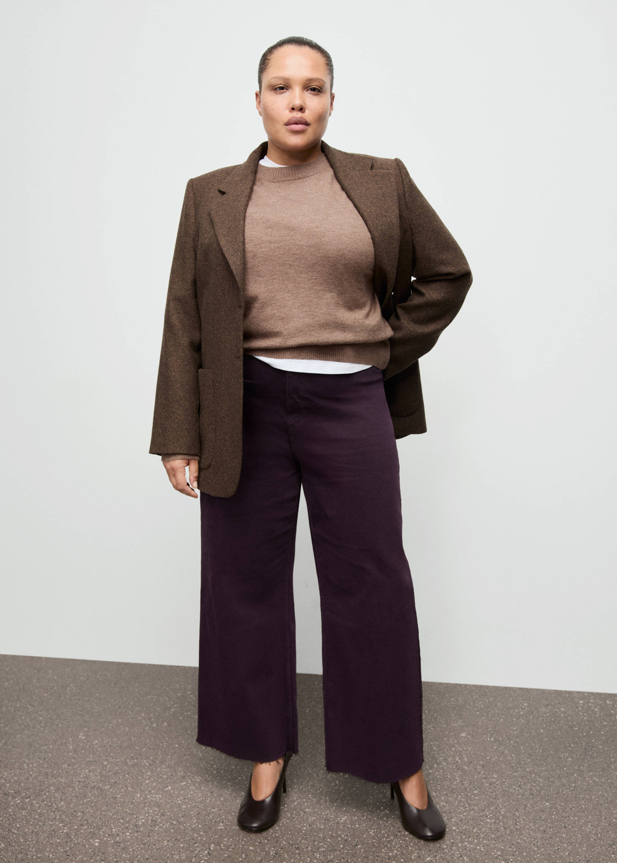Purple wide-leg denim trousers with frayed hems, worn with a brown blazer and sweater.