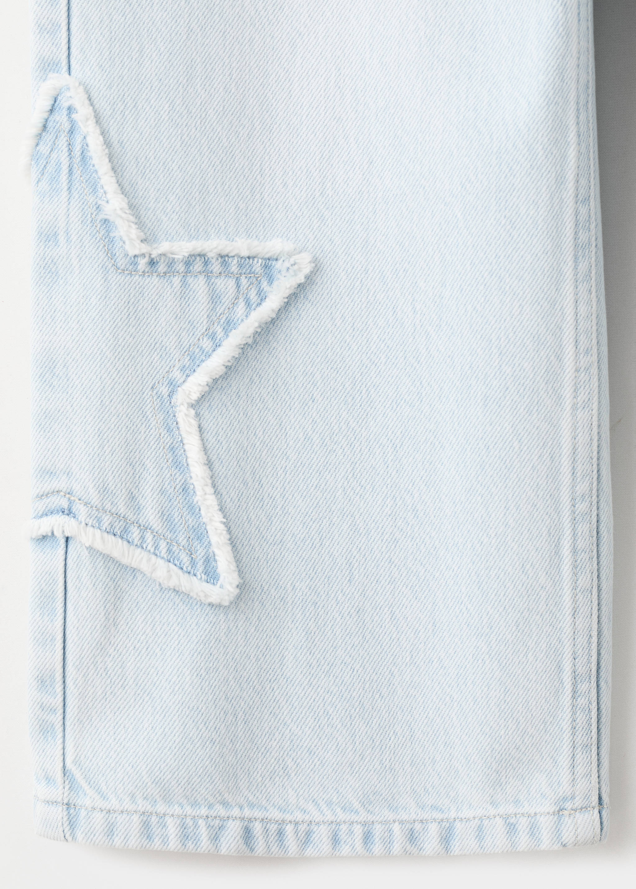 Close-up of light blue denim trousers with a frayed star patch.