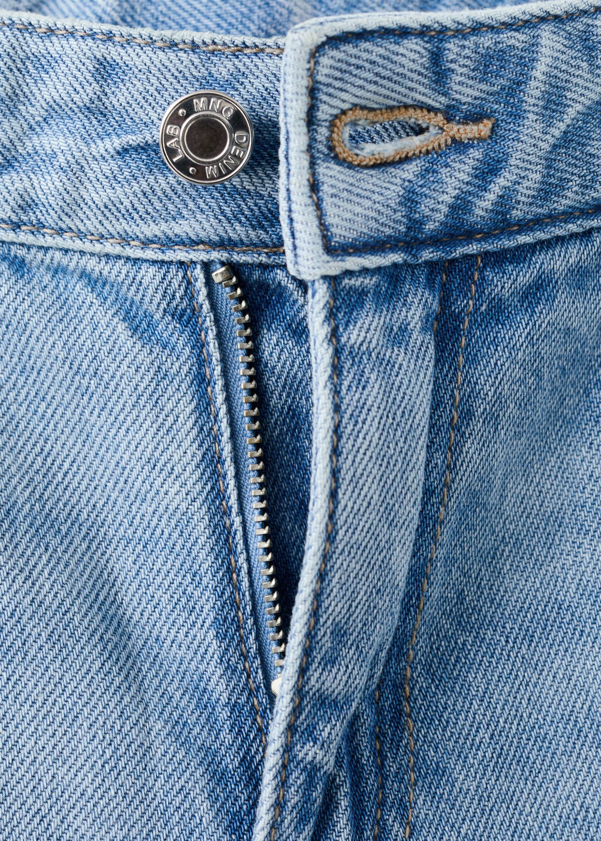 Close-up of light blue denim trousers showing the button and zip closure.