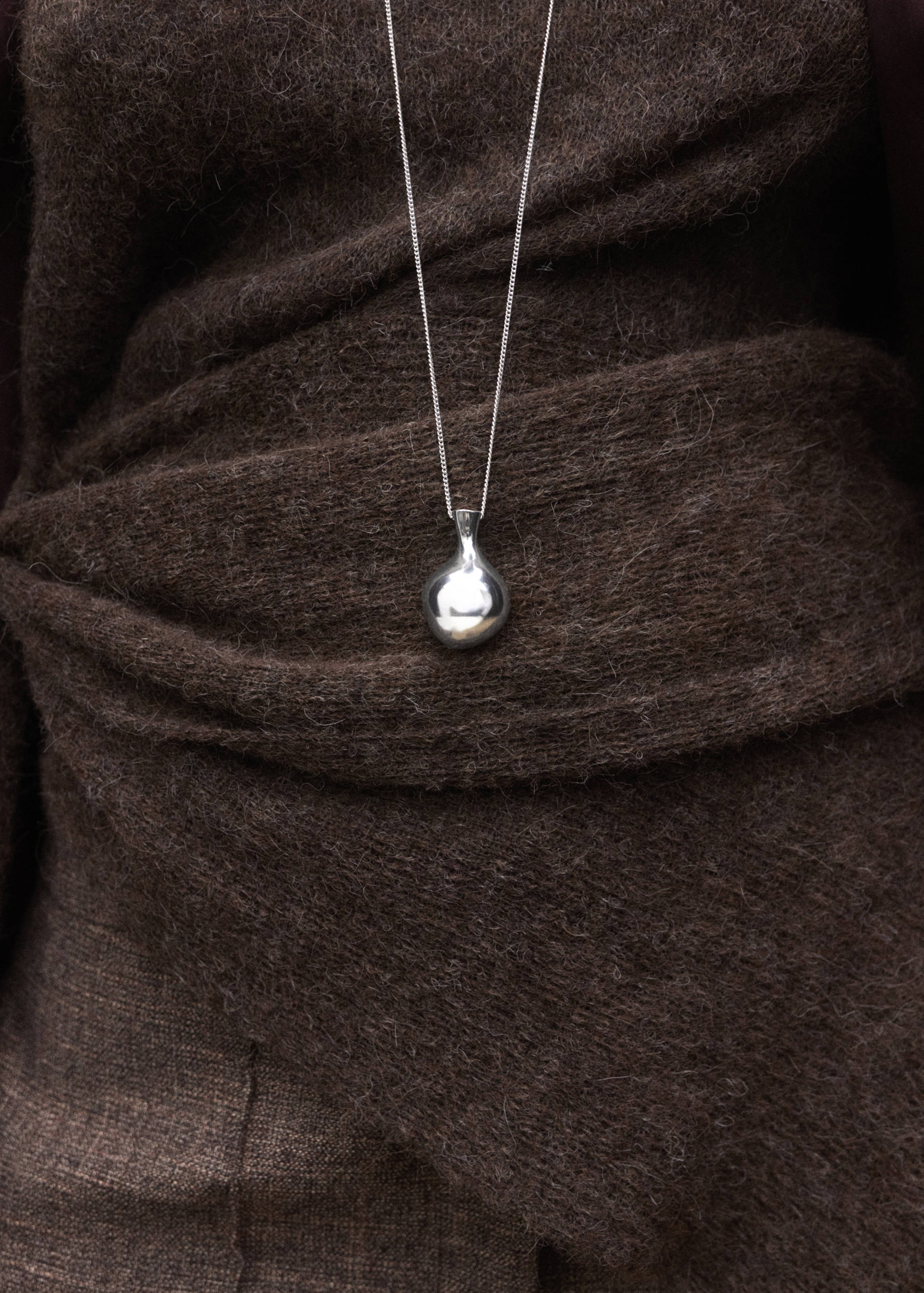Silver pendant necklace with an organic-shaped charm worn over a brown textured wrap top.