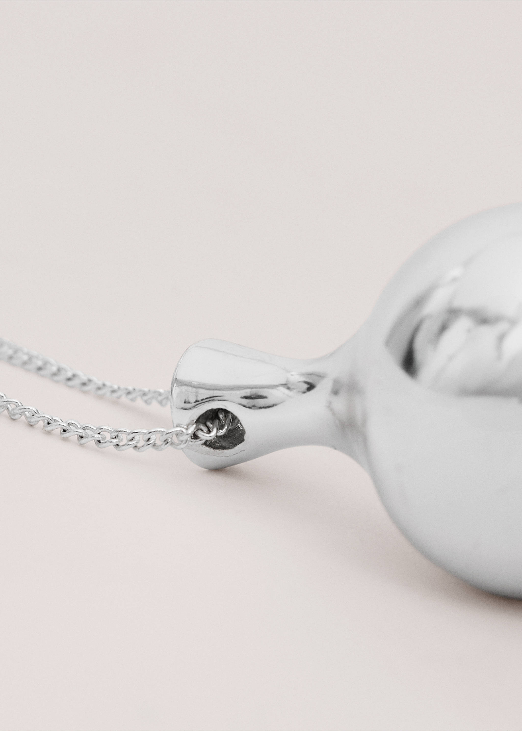 Close-up of a silver metallic pendant on a fine chain., Silver. Ref: 27014446-00.