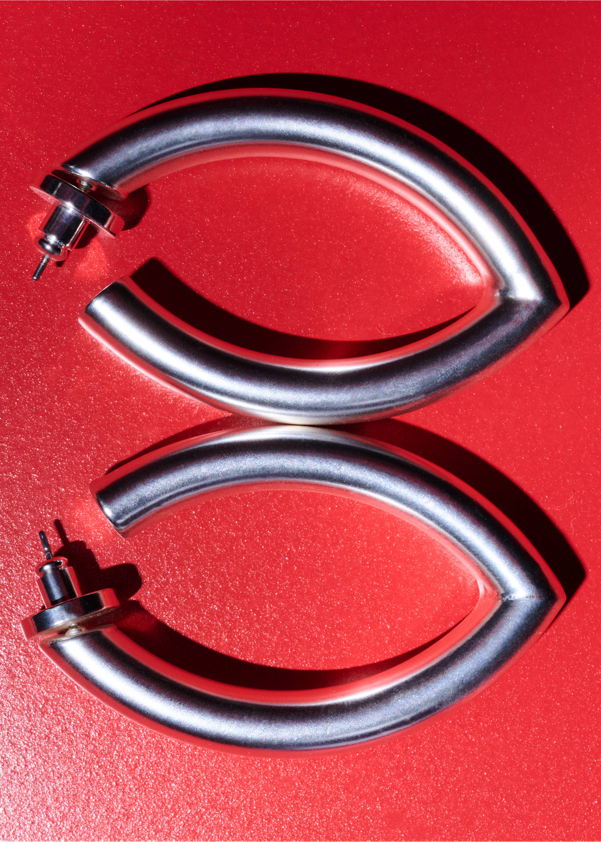 Silver hoop earrings with a chunky, curved geometric design on a red background., Silver. Ref: 27017798-00.
