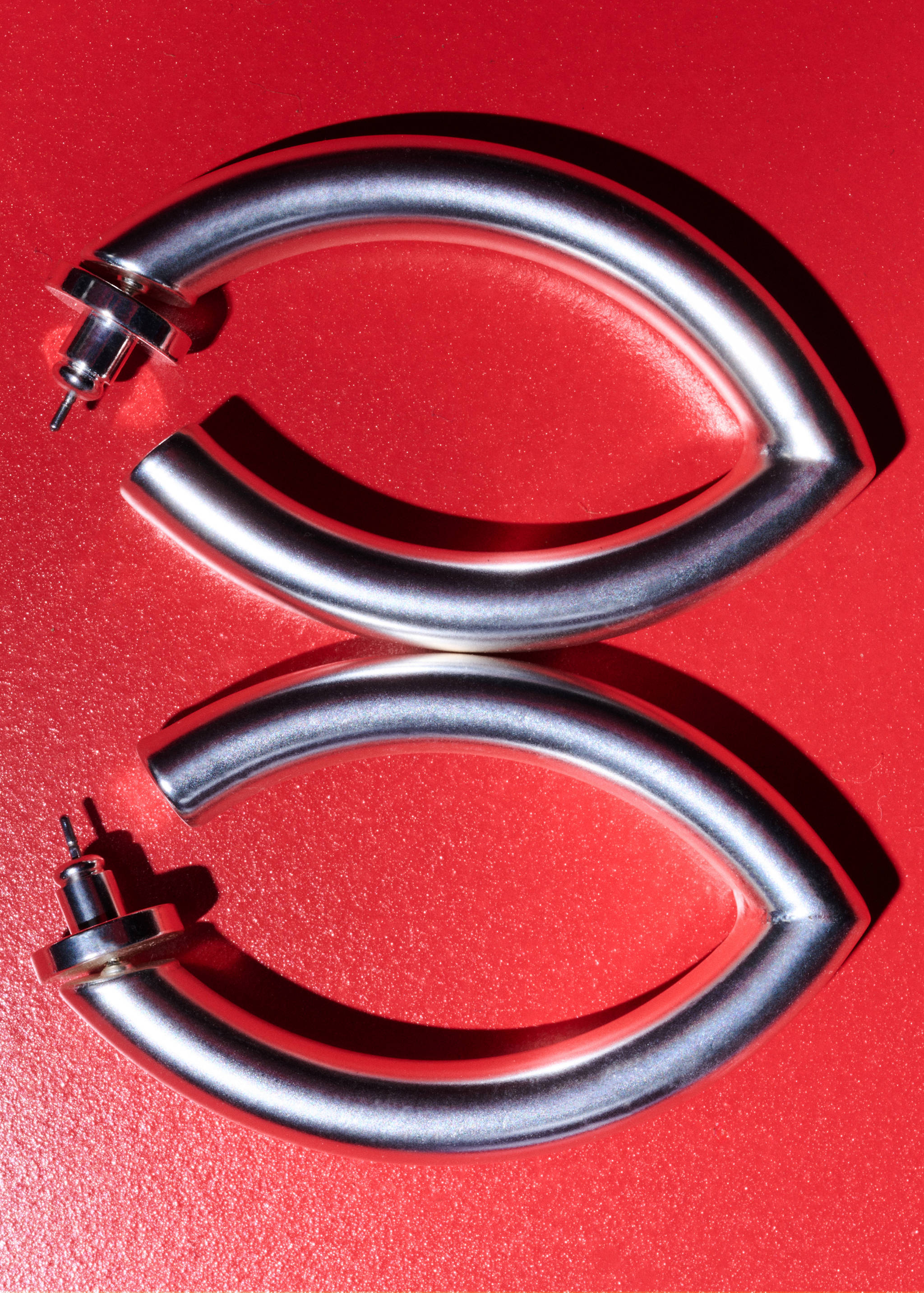 Silver hoop earrings with a chunky, curved geometric design on a red background.
