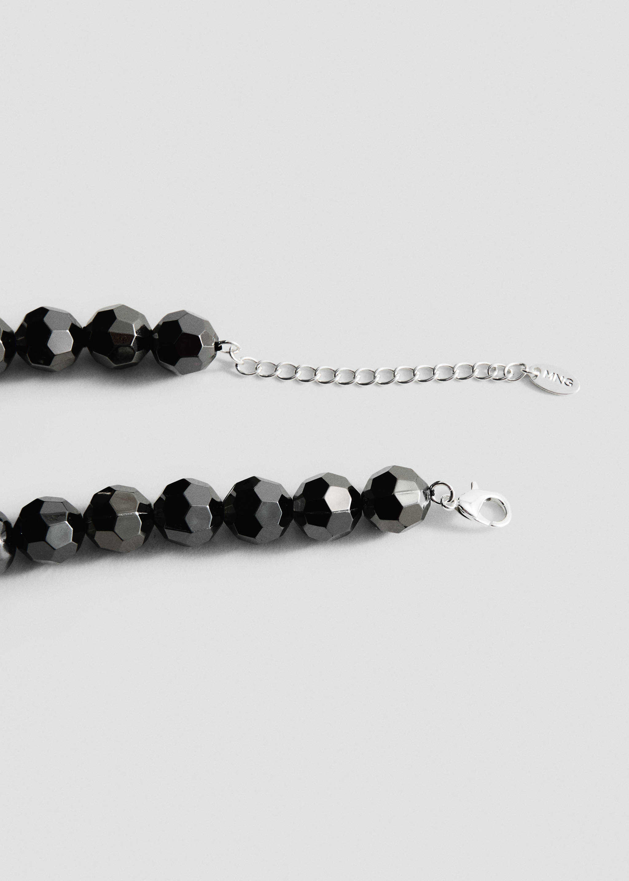 Close-up of a faceted dark metallic beaded collar with a silver-toned chain extender.