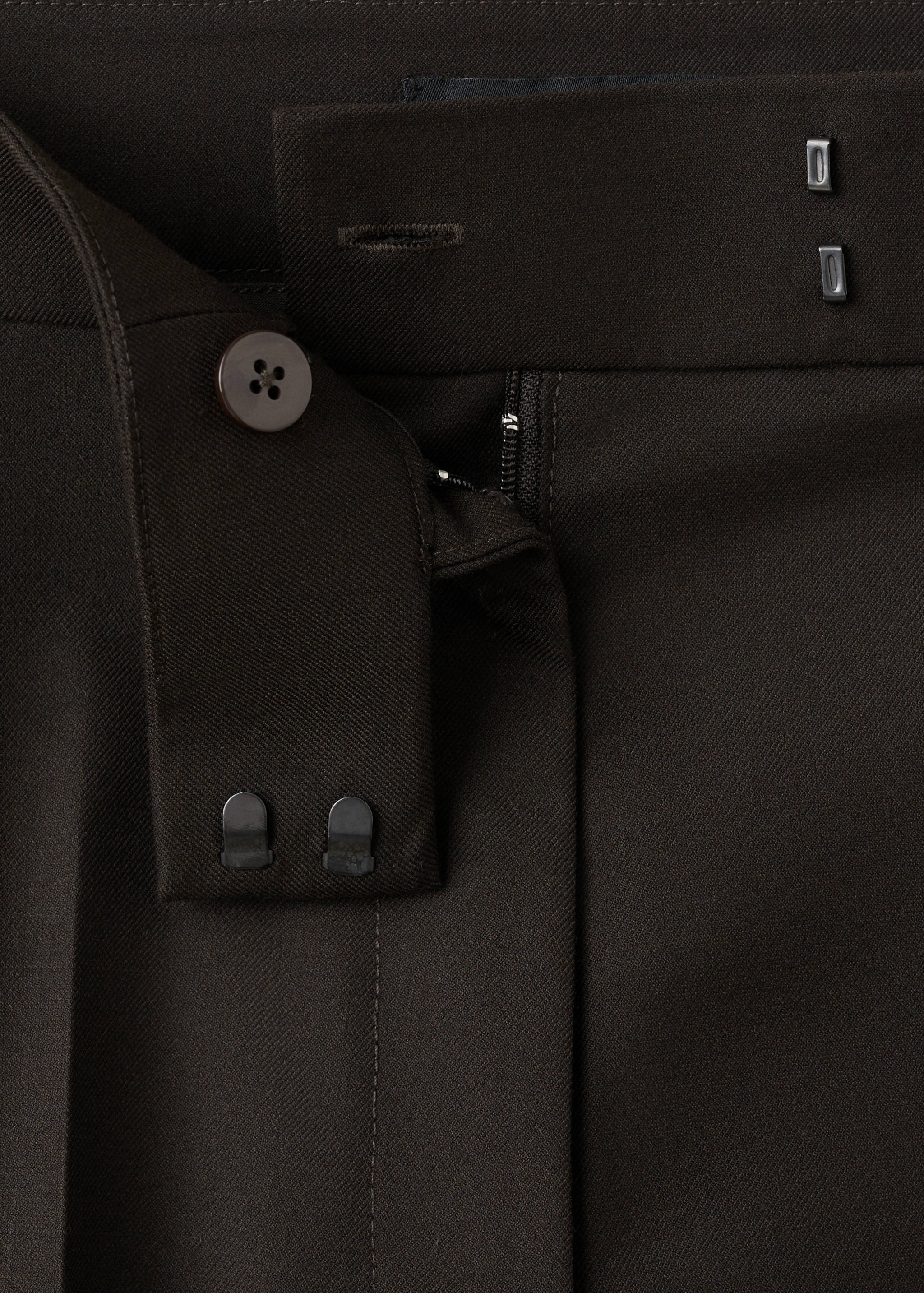 Dark brown trousers waist detail with button and tab closure.