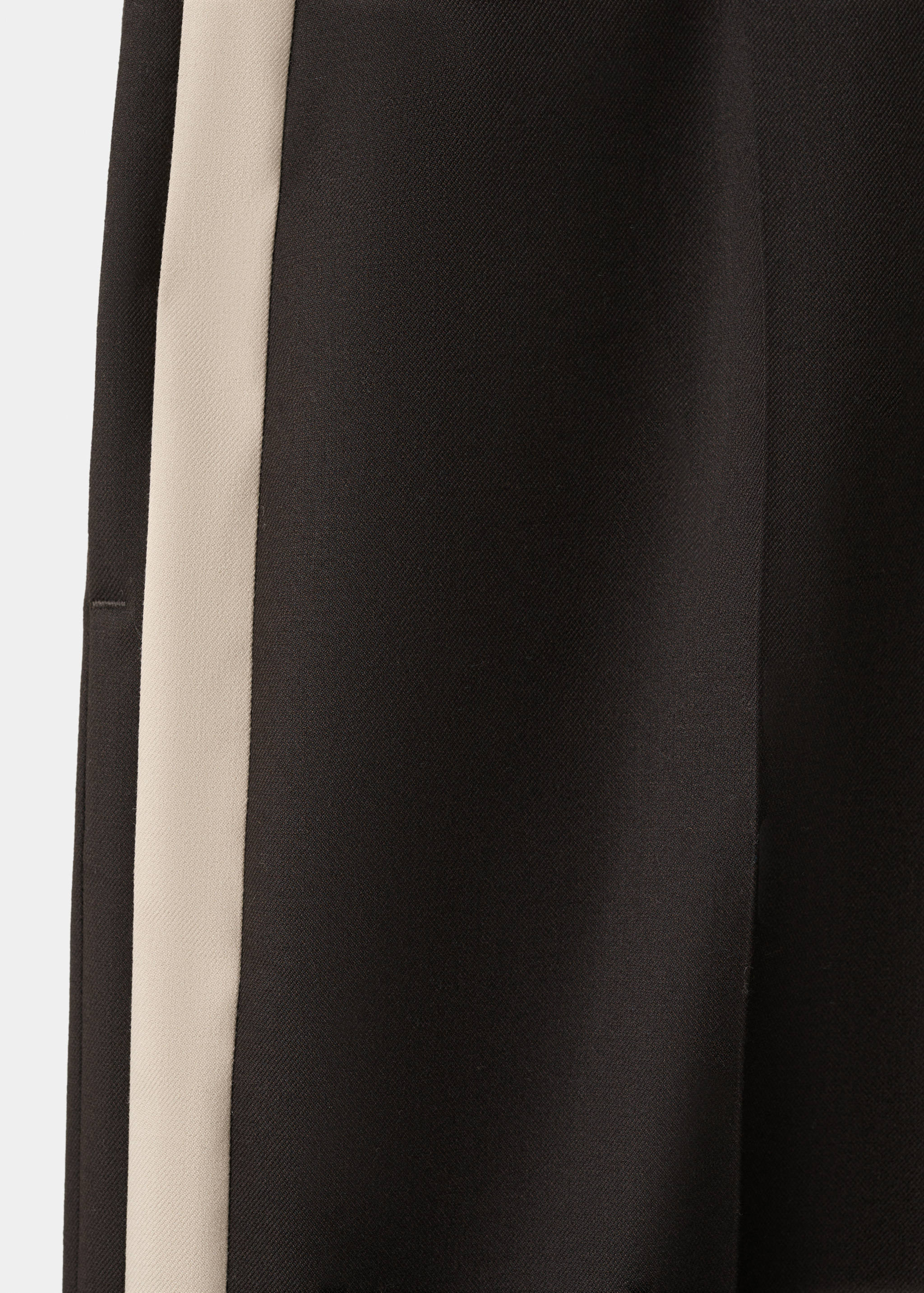 Close-up of black trousers with a wide cream side stripe fabric detail.
