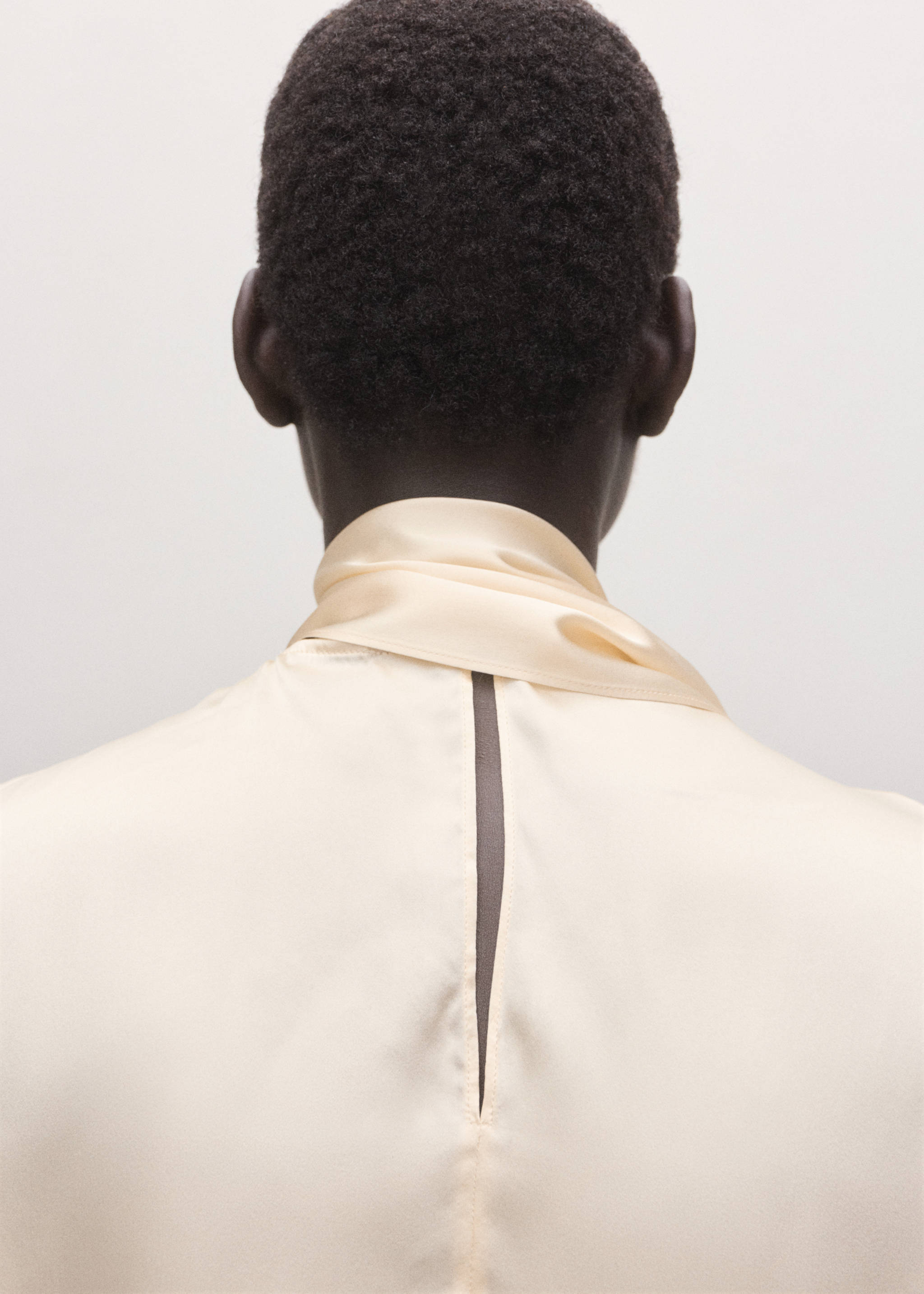 Cream blouse with a satin scarf collar and back slit, back view.