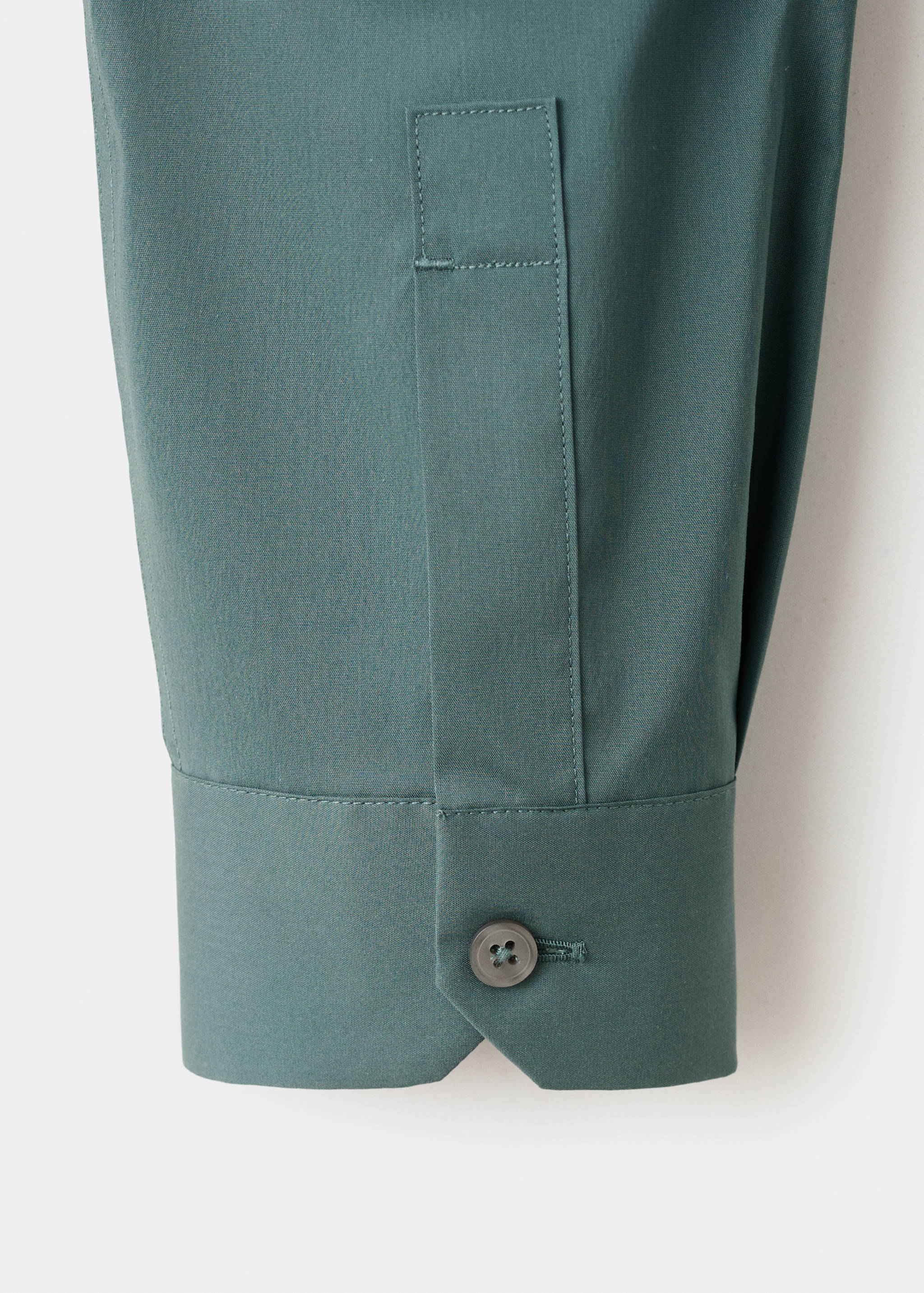 Close-up of the dark green shirt sleeve cuff and button.