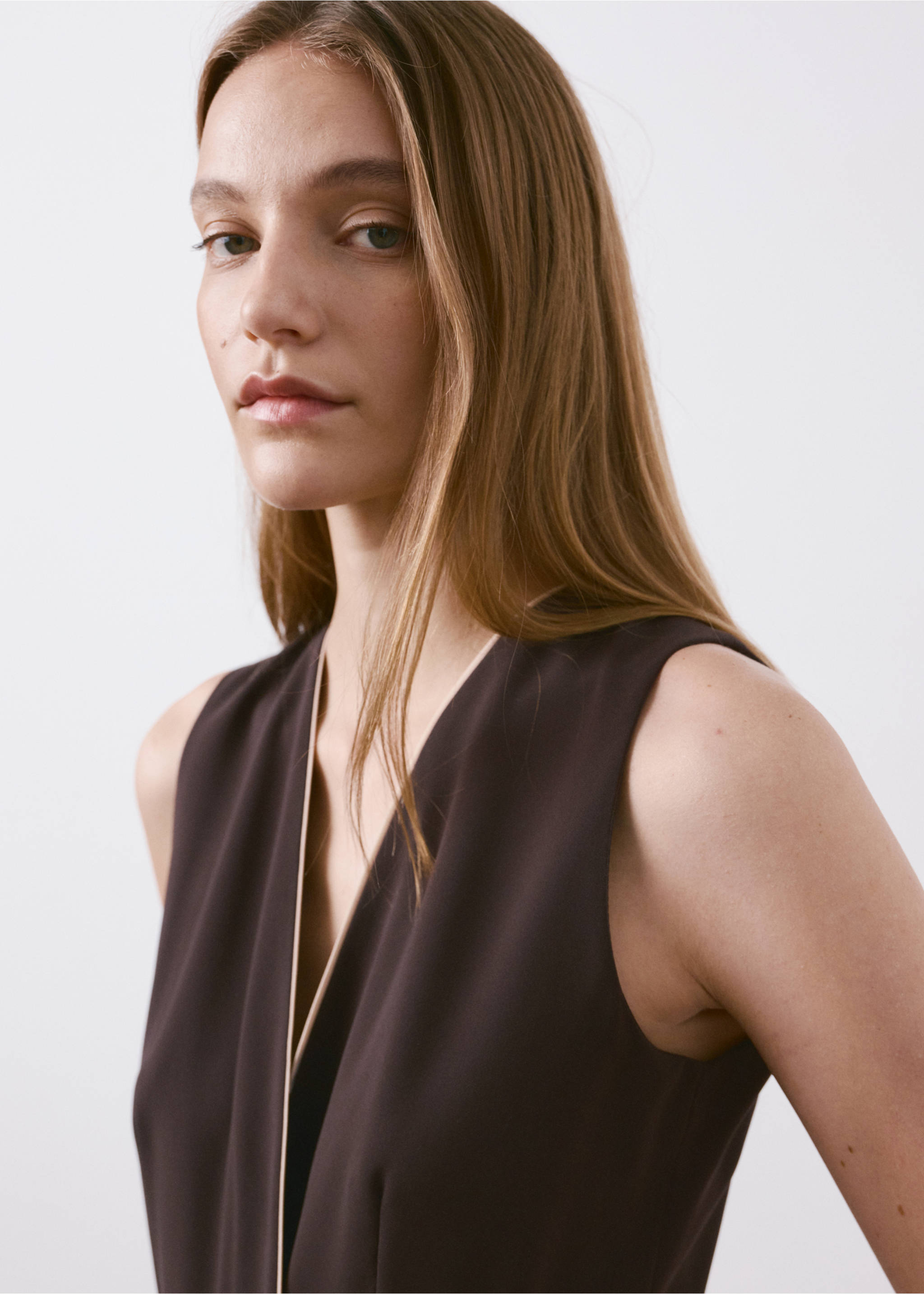 Close-up of a model in a dark brown sleeveless jumpsuit with a V-neck and contrasting piping., Chocolate. Ref: 27025834-00.