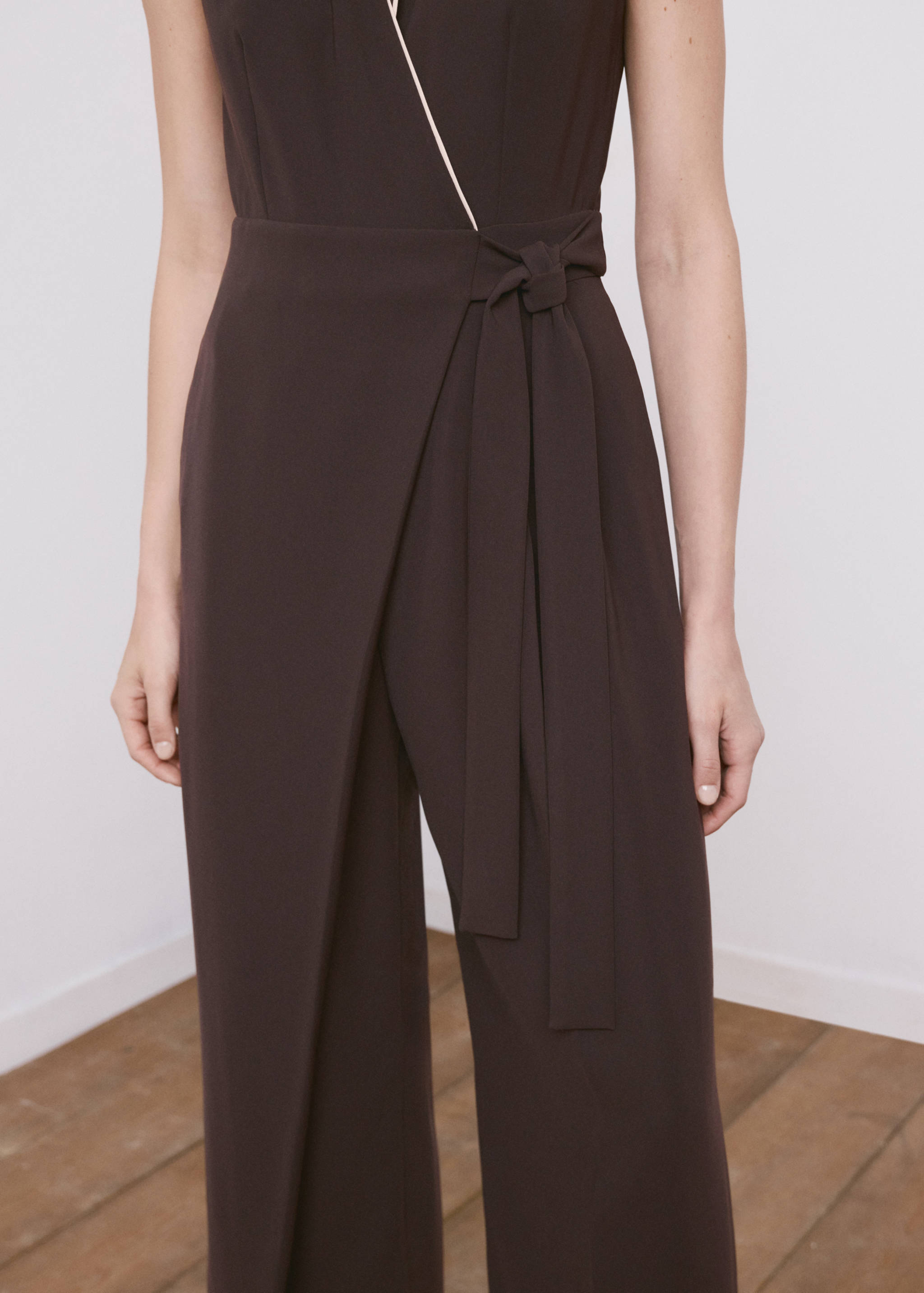 Dark brown sleeveless jumpsuit with a wrap neck and tie-belt.