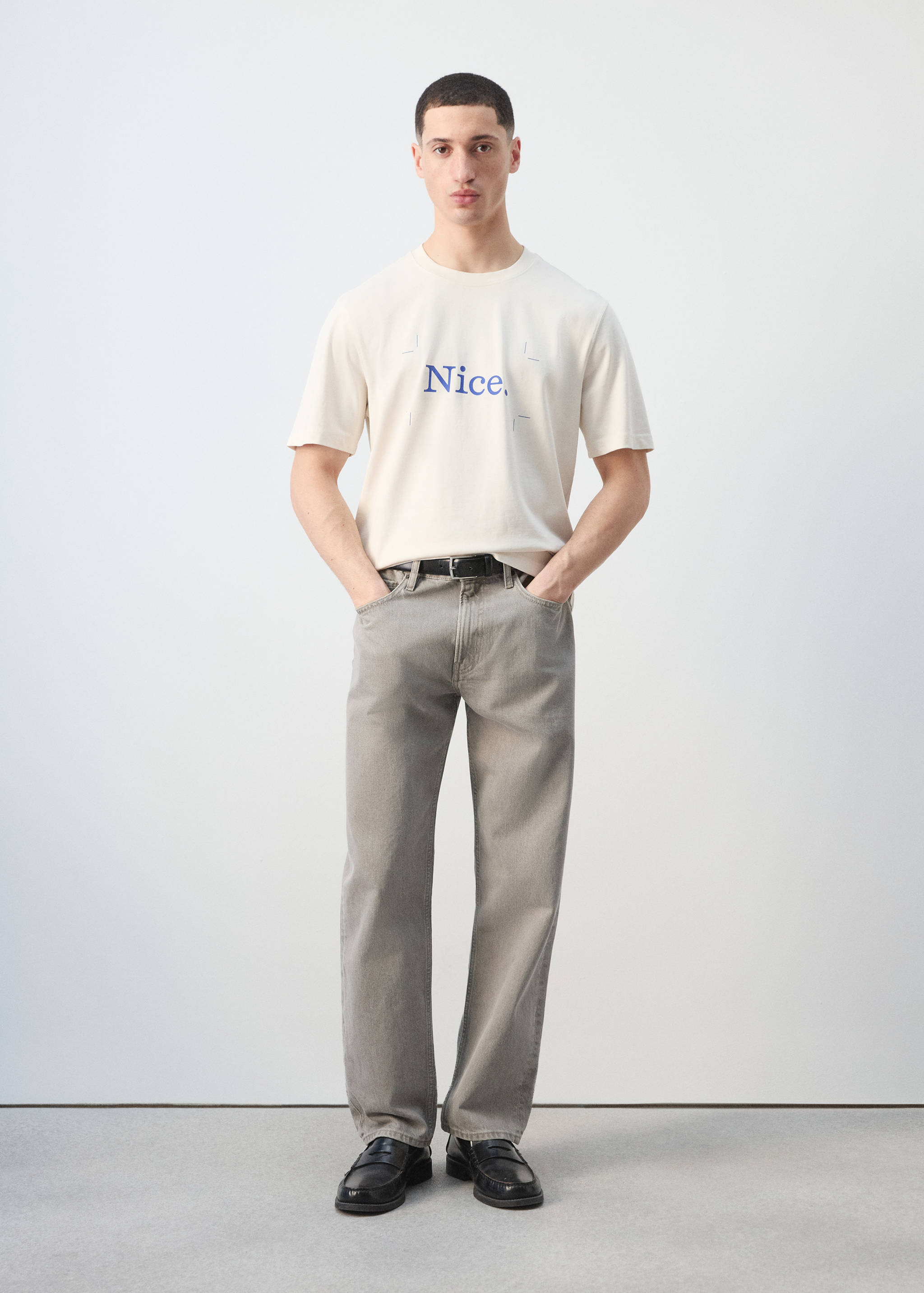Off-white short-sleeved t-shirt with blue chest text, worn with grey trousers.
