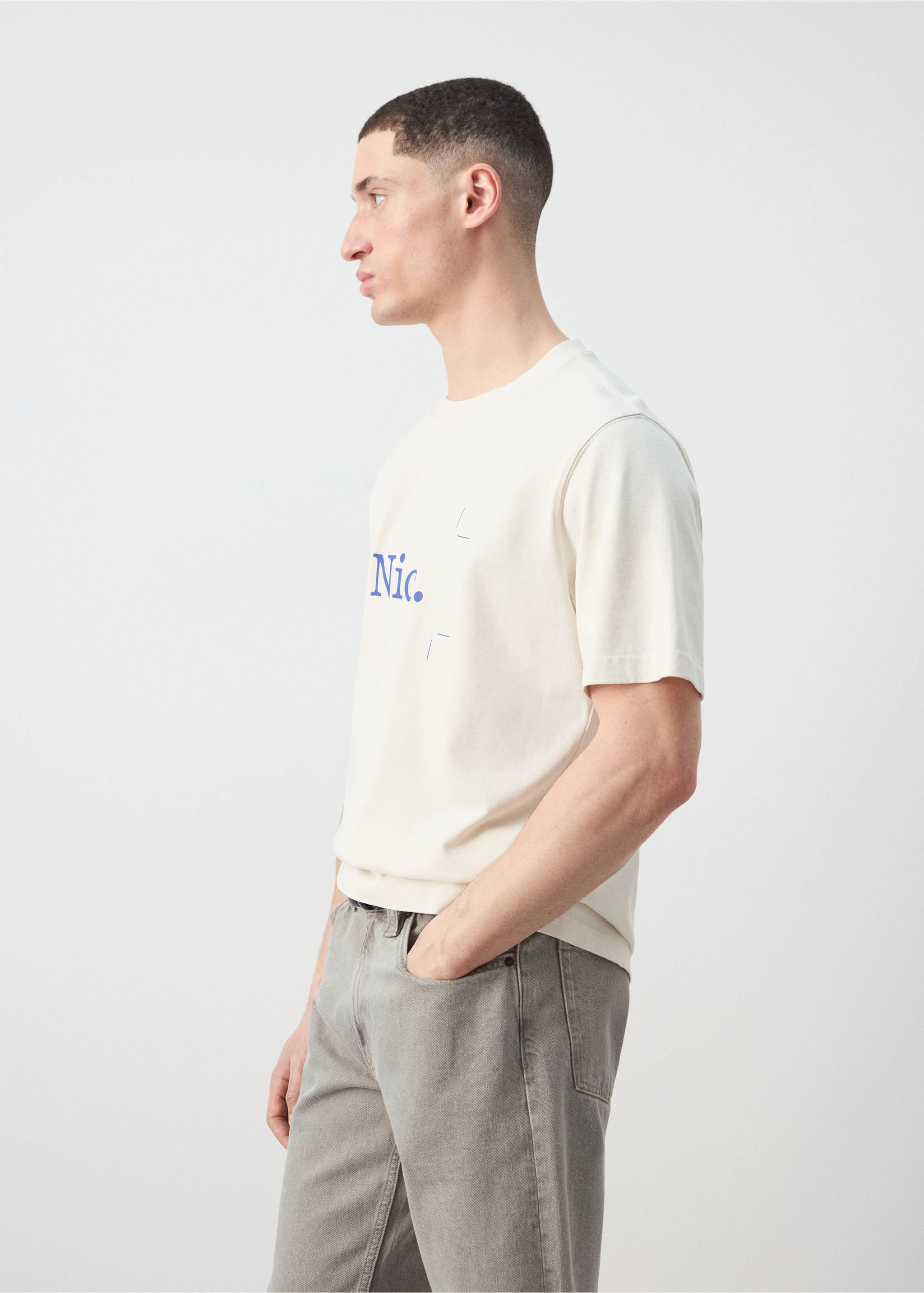 Cream short-sleeved t-shirt with blue chest graphic, worn with grey trousers., Off White. Ref: 27025993-00.