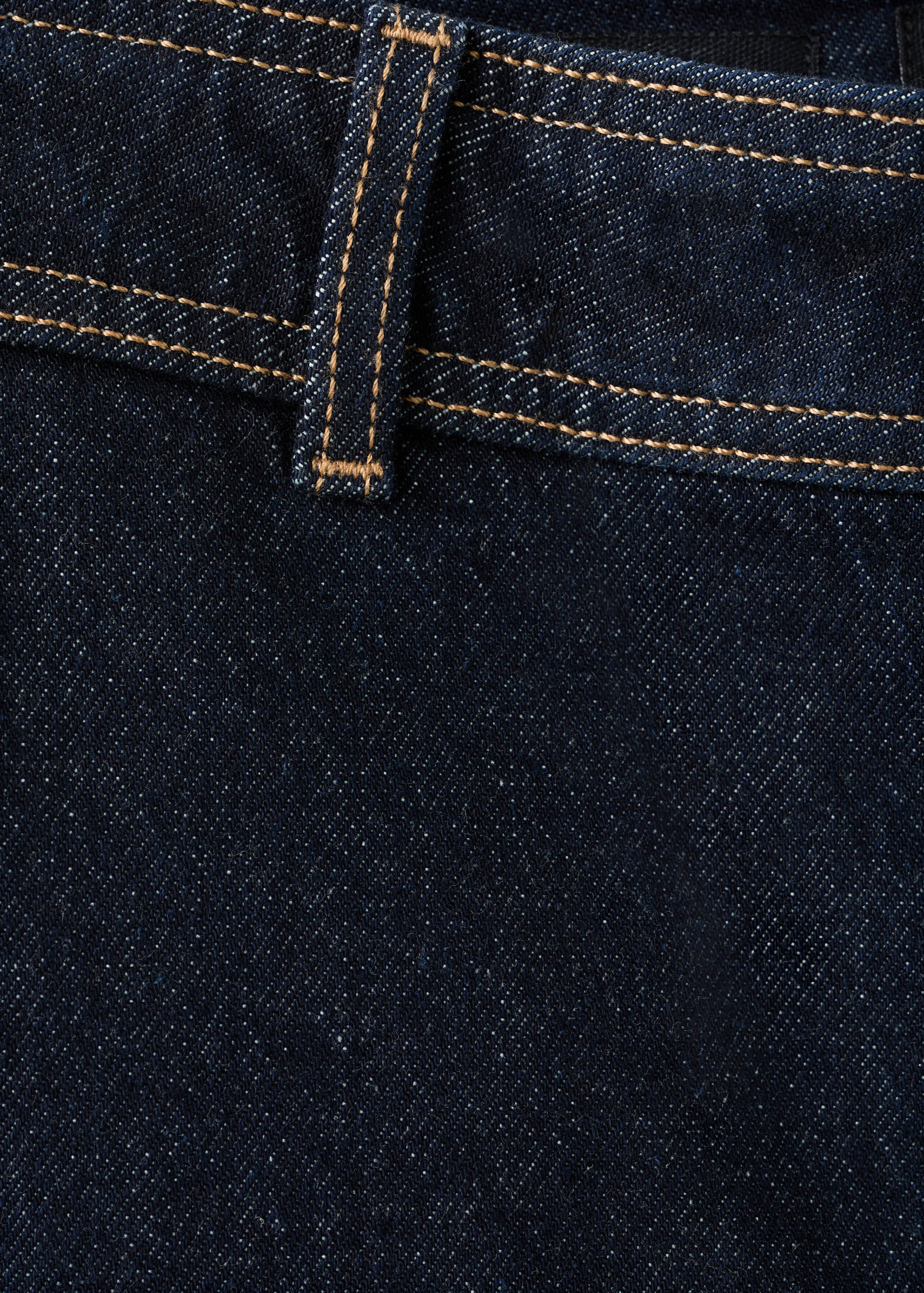 Close-up of dark blue denim fabric with contrast topstitching and a belt loop.