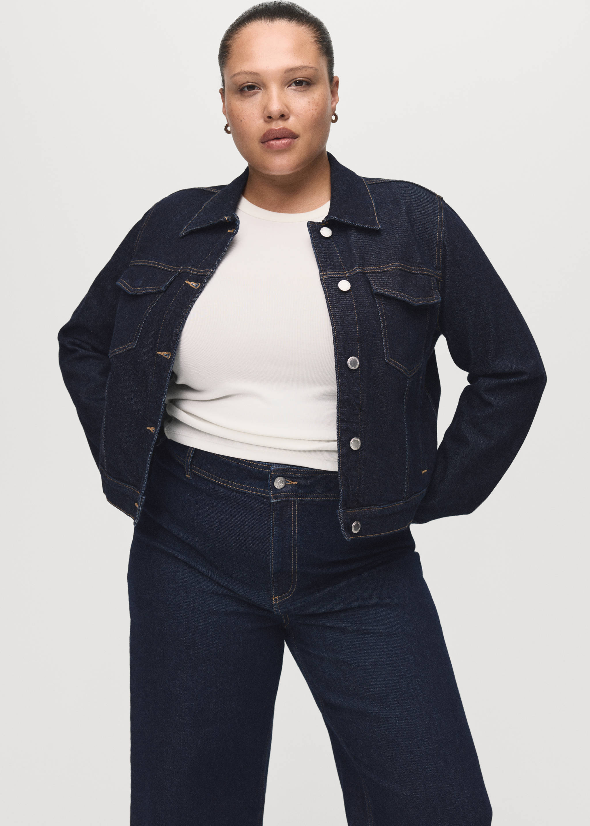 Dark blue denim jacket with silver buttons and chest pockets, worn over a white top.