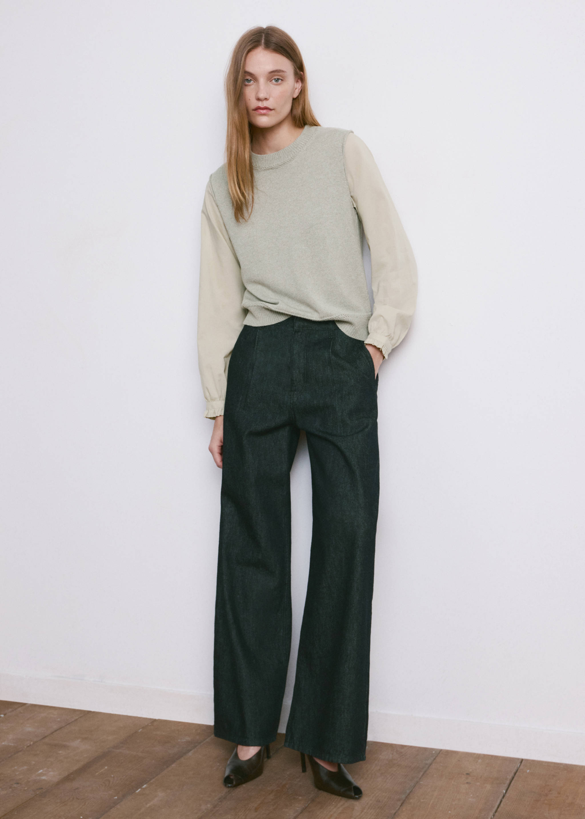 Light green knit jersey sweater vest with long sleeves, worn with dark wide-leg trousers.