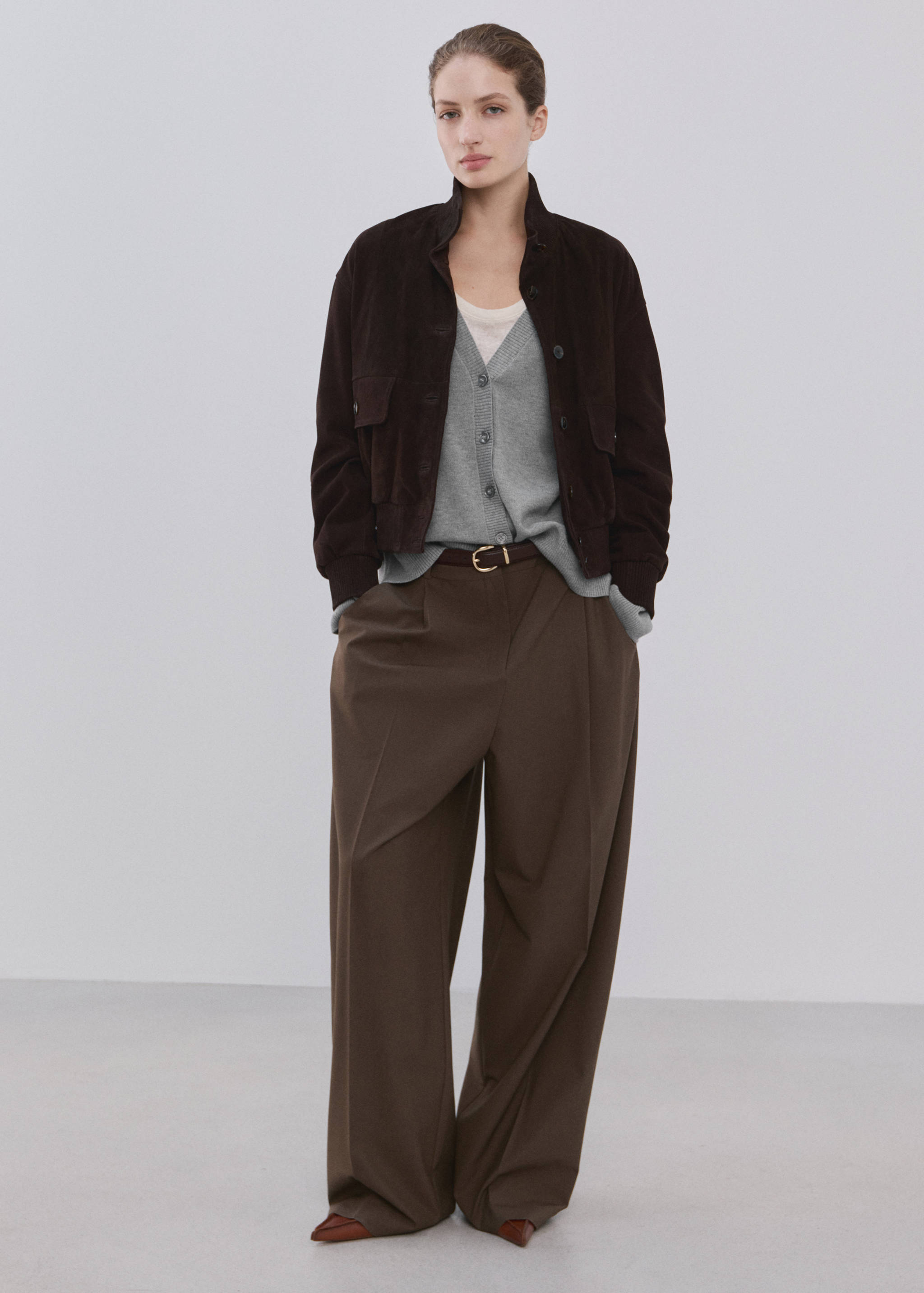 Grey V-neck cardigan worn under a dark brown jacket with trousers.