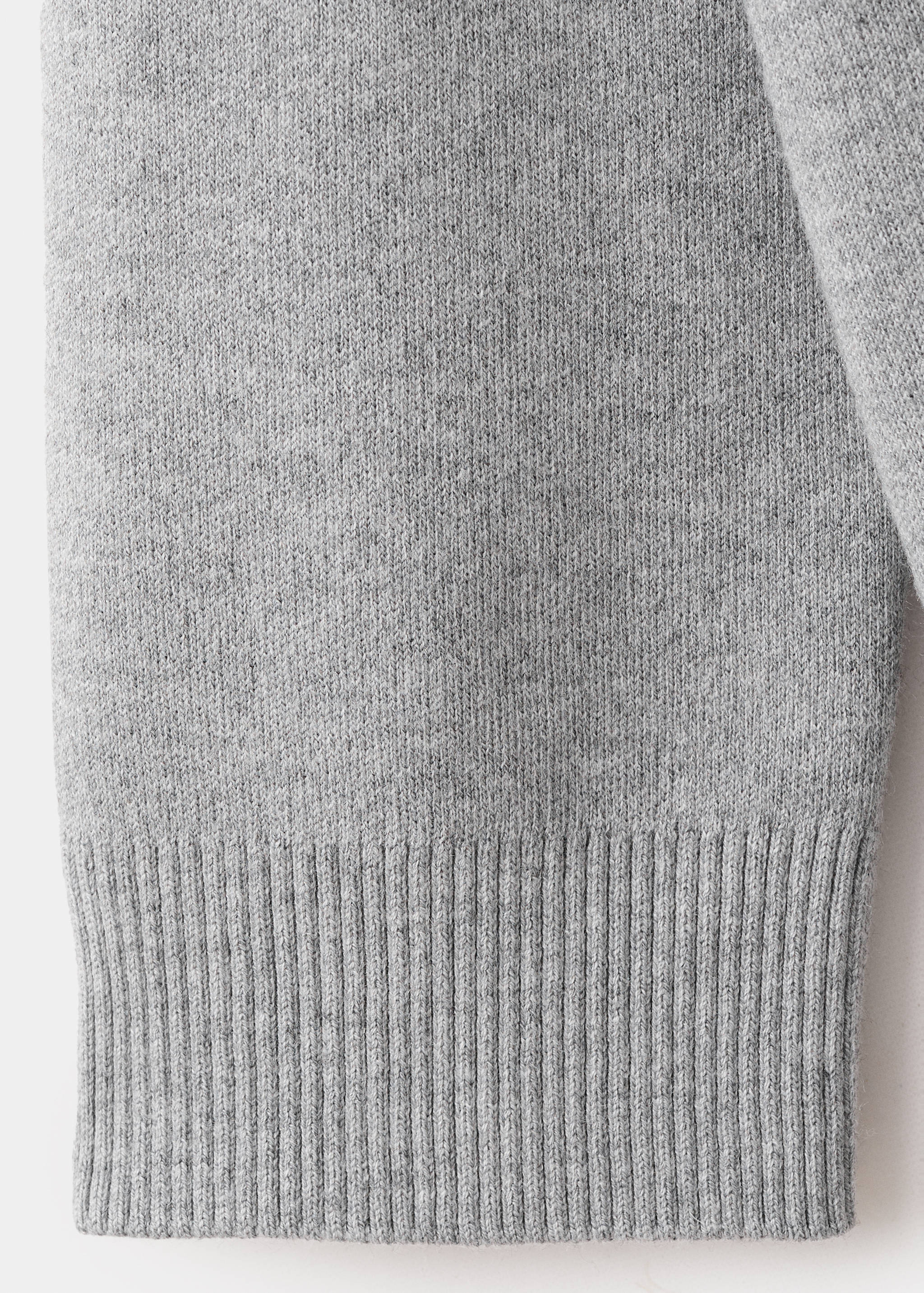Close-up of the grey knitted fabric and ribbed hem of a cardigan.