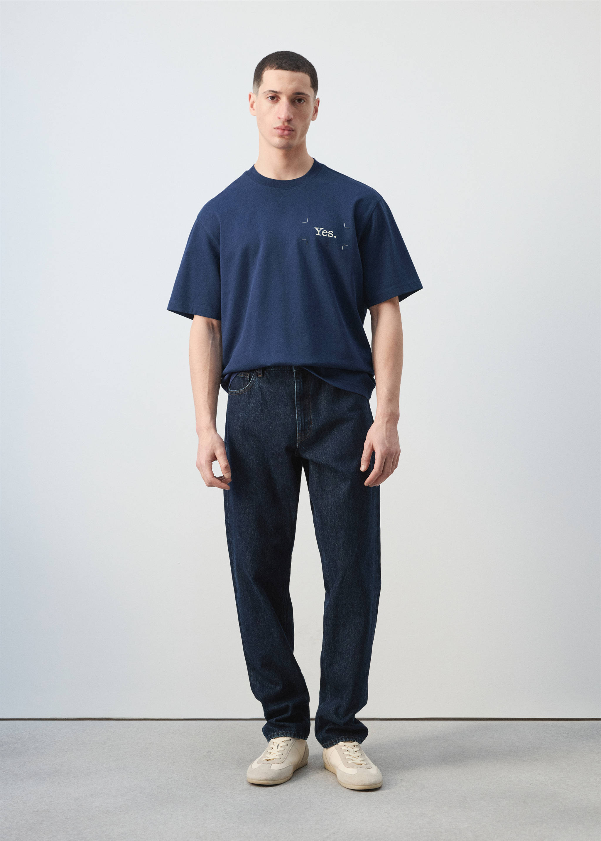 Navy blue short-sleeved t-shirt with a small white chest text print, worn with dark denim trousers.