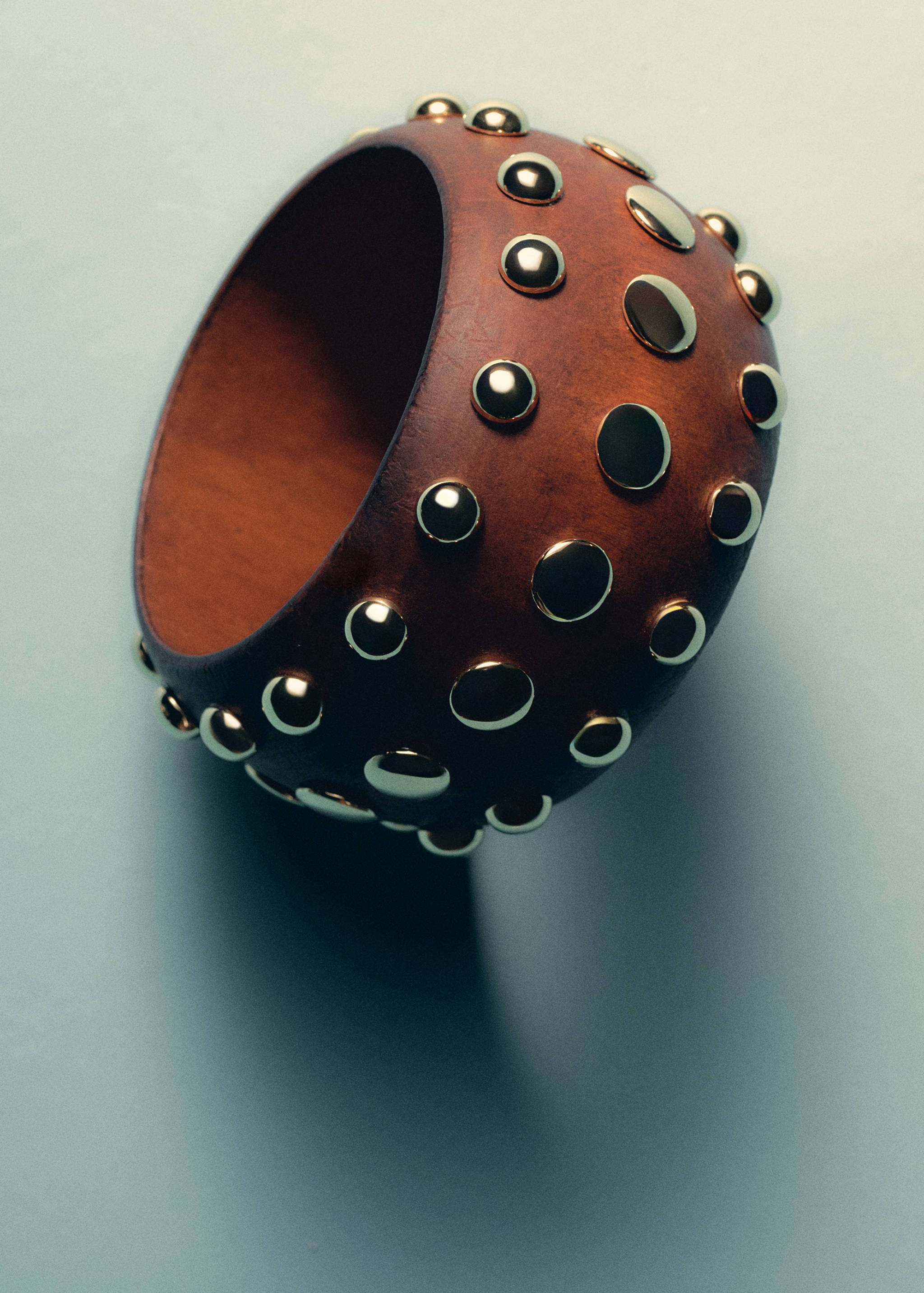 Brown rigid bangle bracelet studded with polished gold-coloured dome studs.