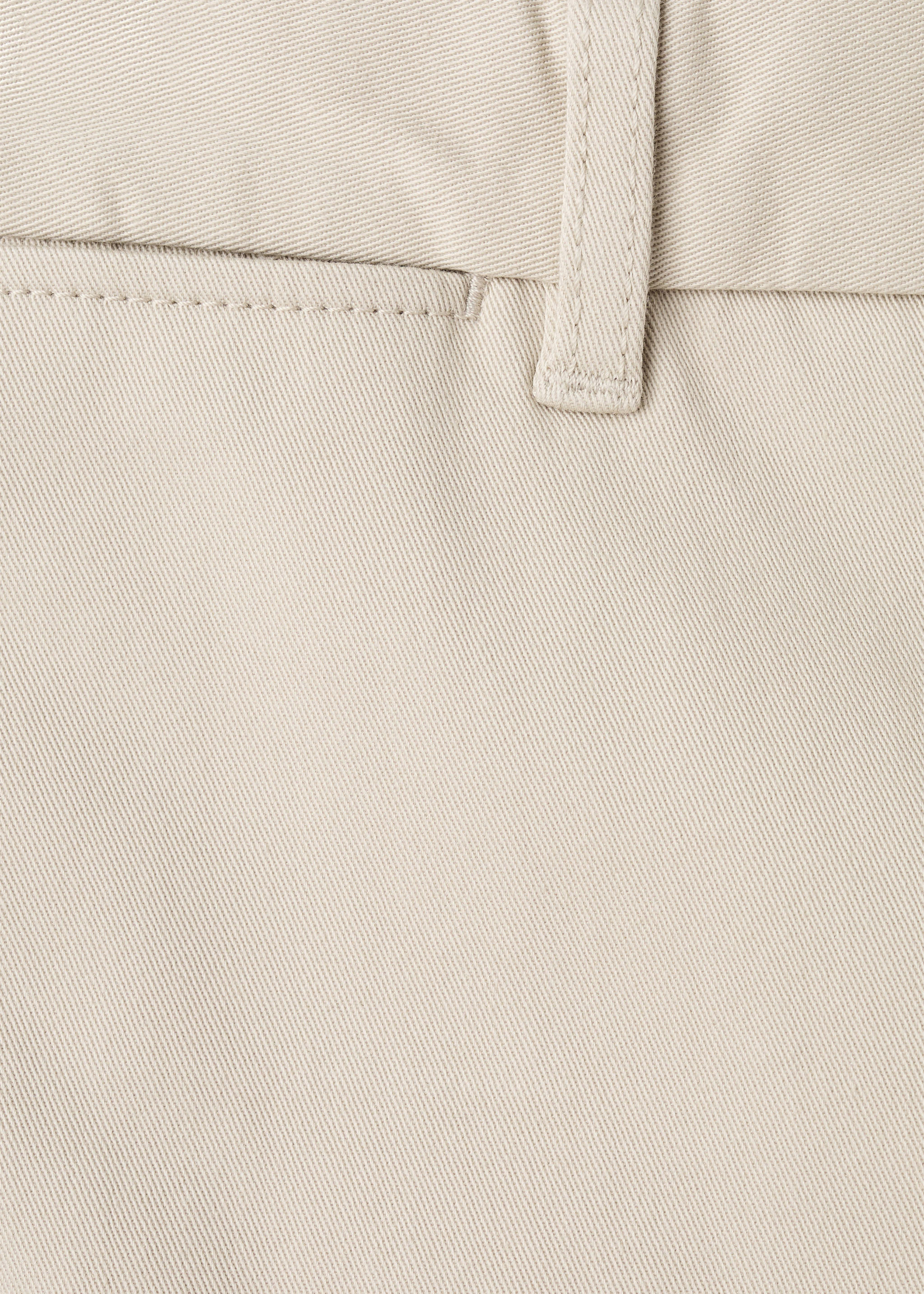 Close-up of beige men's trousers showing fabric texture and belt loop detail.
