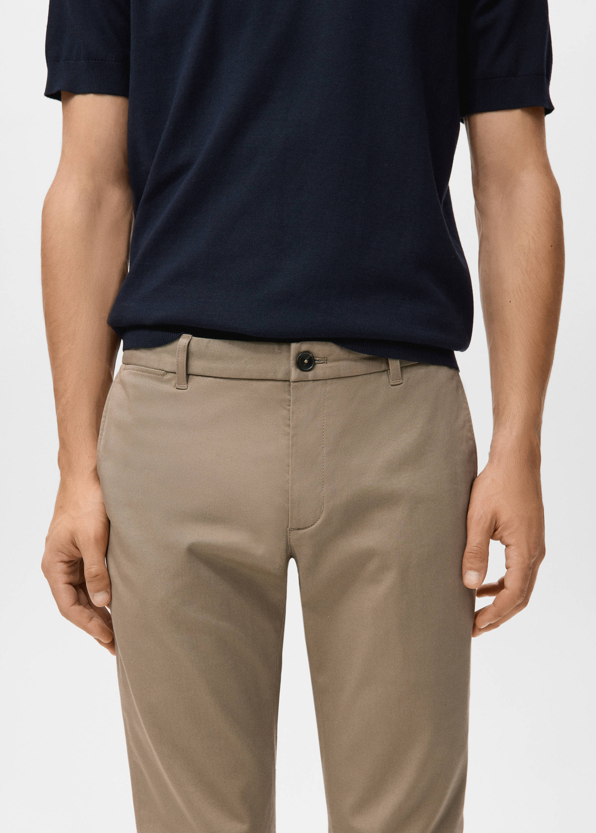 Taupe trousers with belt loops and button closure, worn with a navy blue knit top.