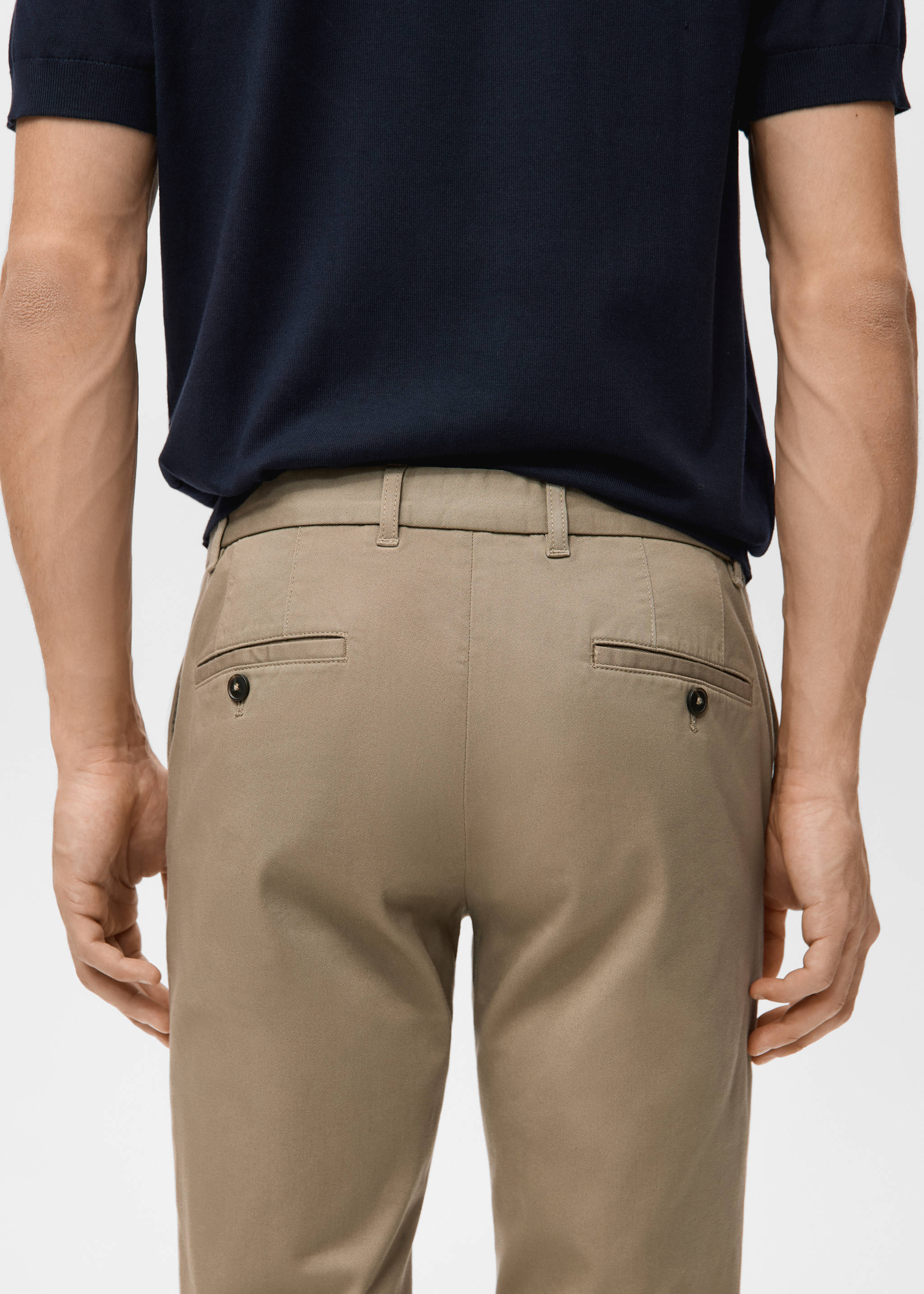 Beige trousers with back buttoned welt pockets, worn with a dark navy polo shirt
