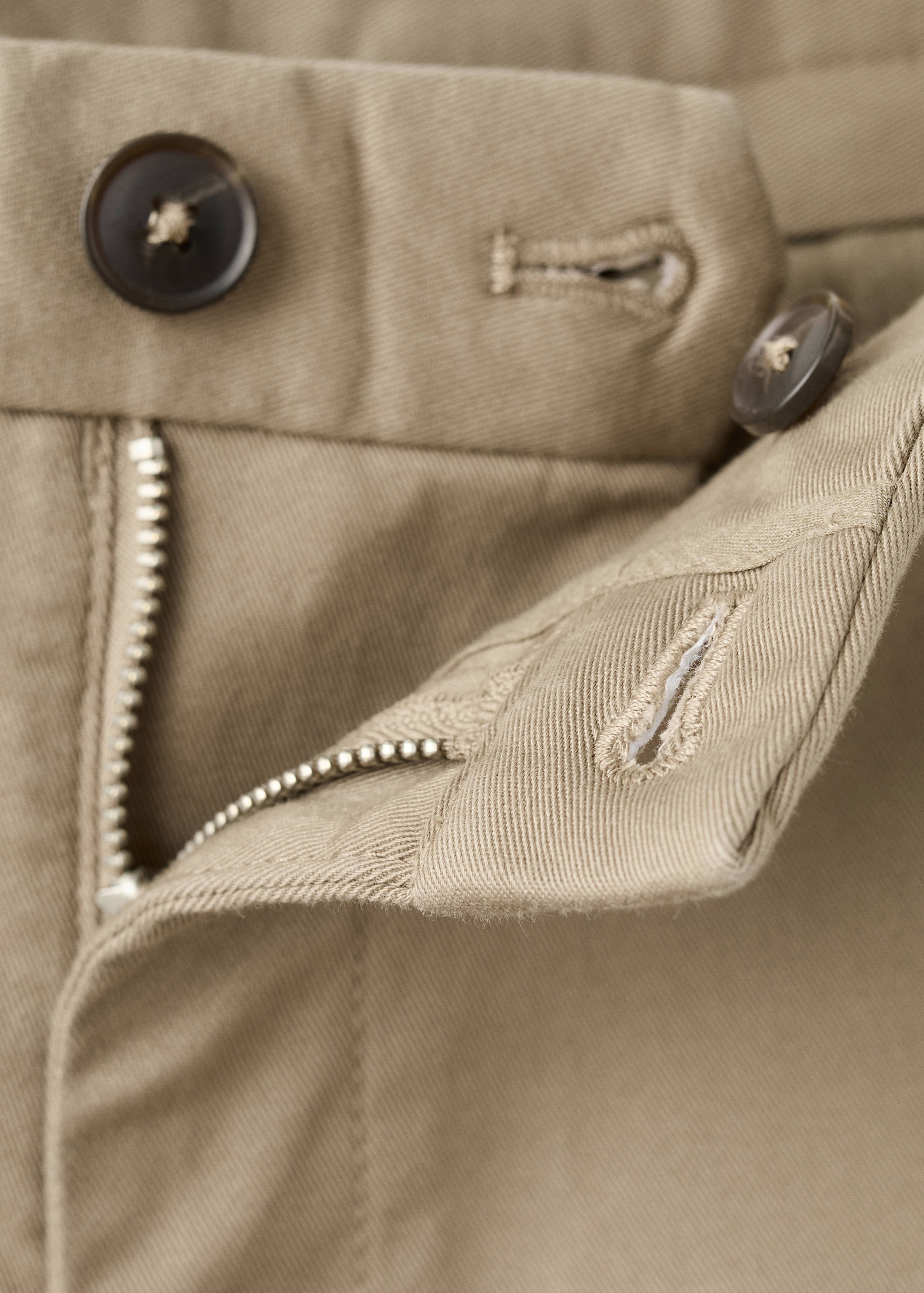 Close-up of beige men's trousers showing the waistband and zip fly detail.